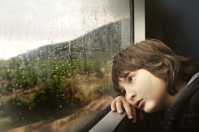 Boy looks out window as rain falls | Photo: Pixabay