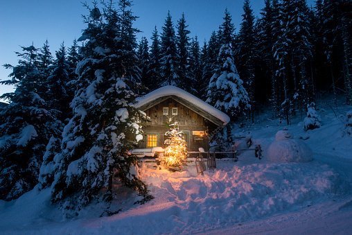 Snowman and Christmas tree at illuminated wooden house in snow at night | Photo: Getty Images