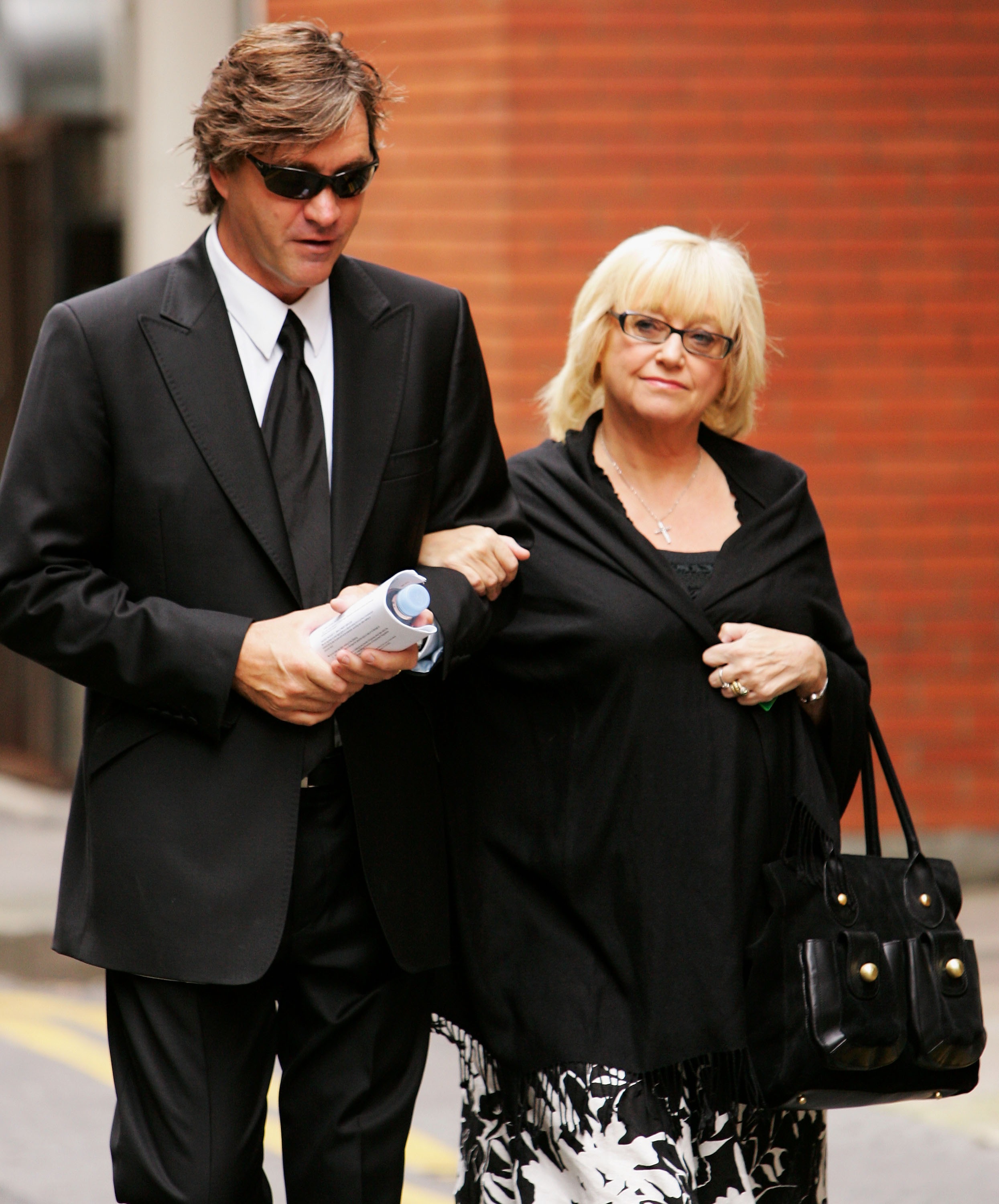Judy Finnigan and Richard Madeley are seen arriving at the funeral of Tony Wilson in Manchester on 20 August 2007, dressed in sombre black as they walk arm in arm — a quiet, reflective moment that contrasts with their usual public appearances, underscoring their close ties within the broadcasting community.