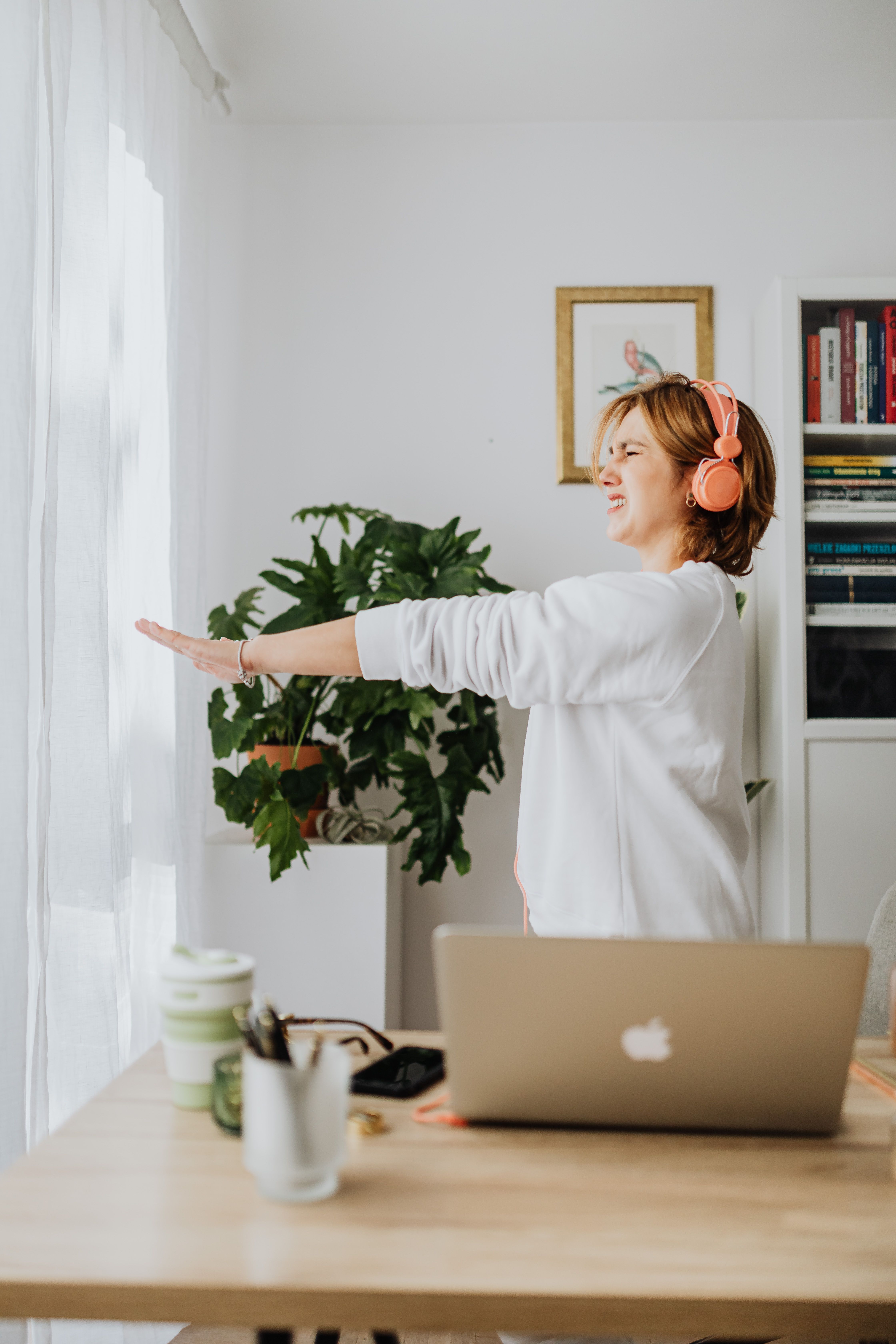 A woman wearing headphones stretches her arms beside her laptop. | Source: Pexels