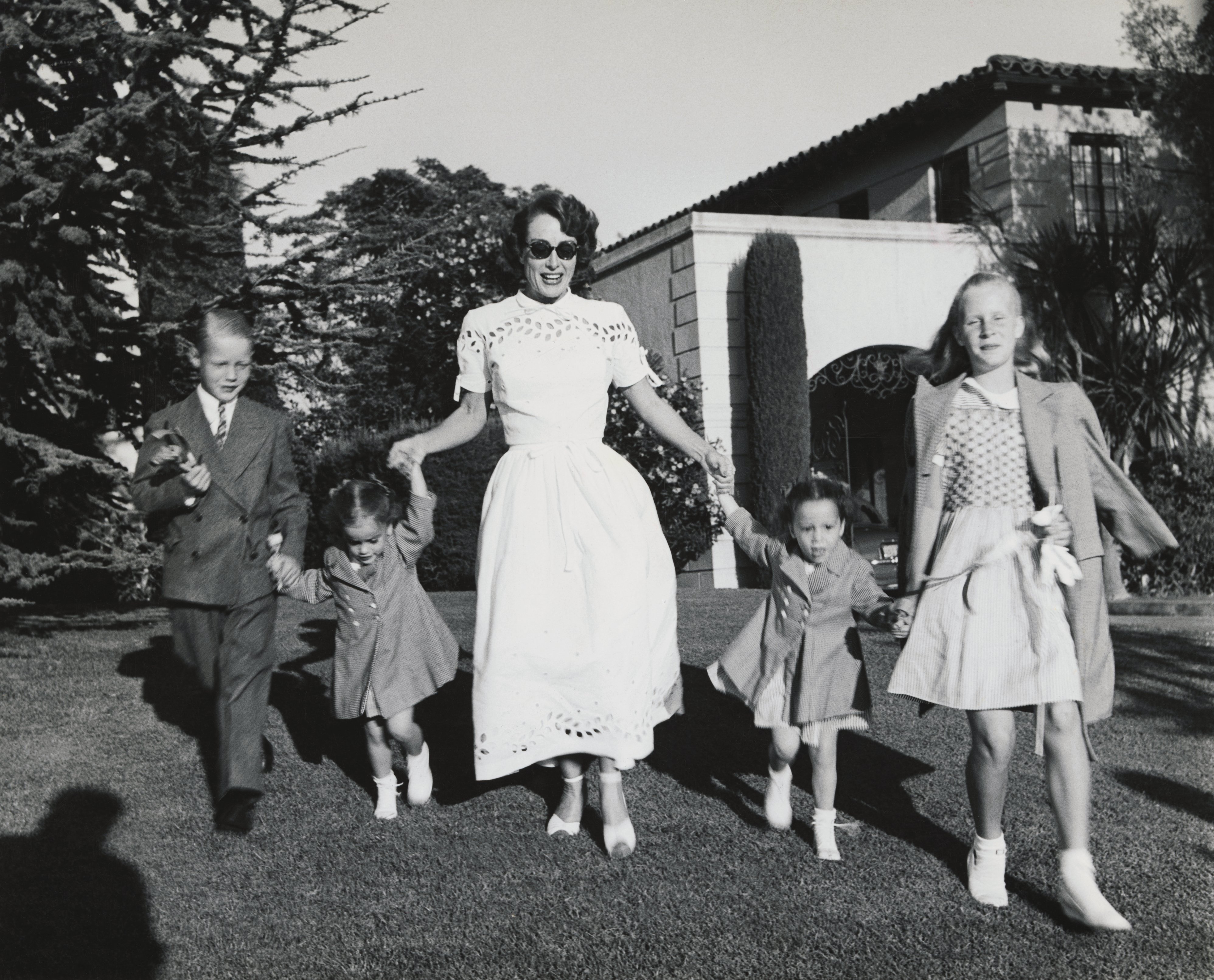 Joan Crawford and four children, Christopher, Cathy, Cynthia, and Christina romp on lawn following party given by Ann Rutherford for daughter Gloria's 5th birthday. | Source: Getty Images