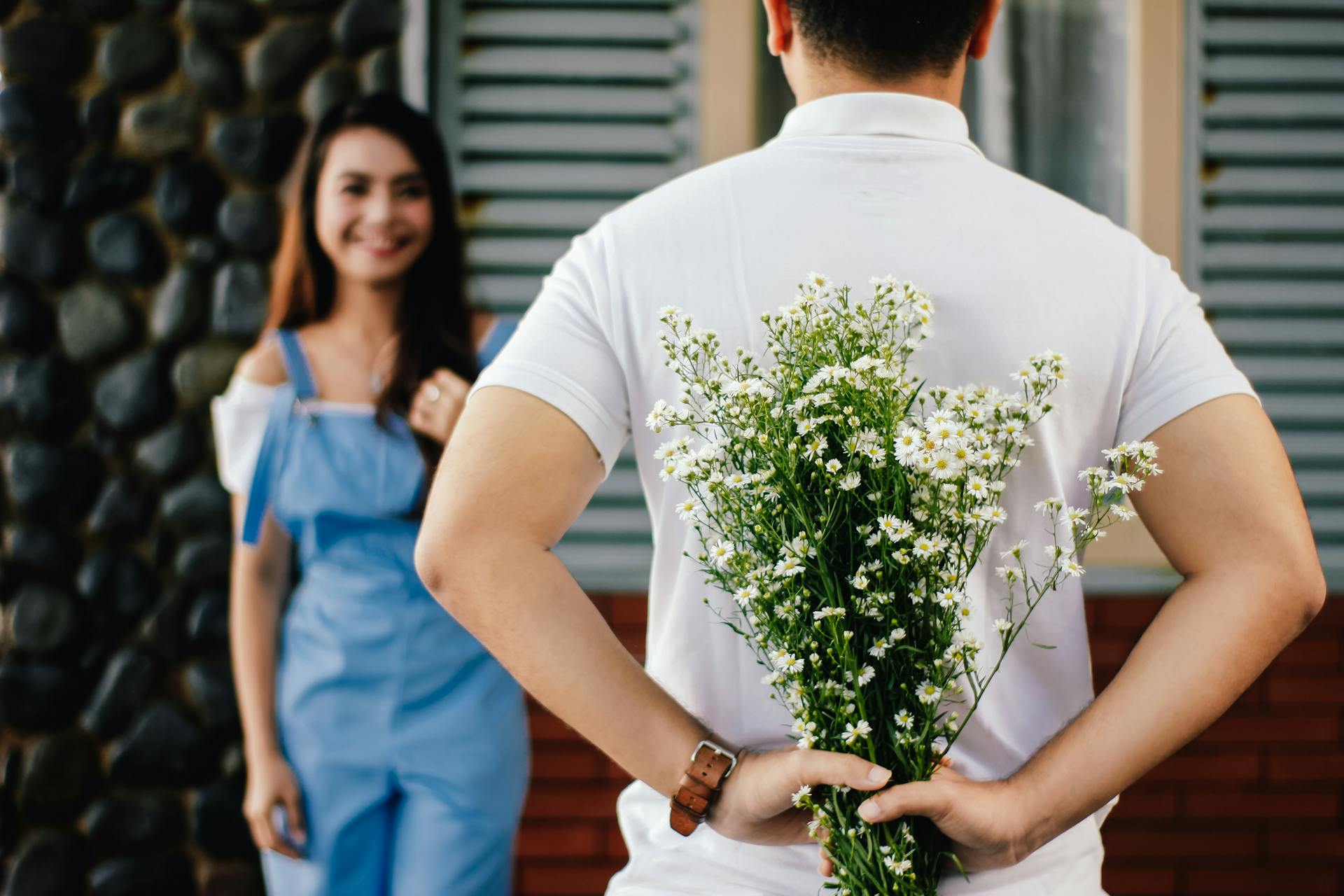 A man hiding flowers behind his back for his girlfriend | Source: Pexels