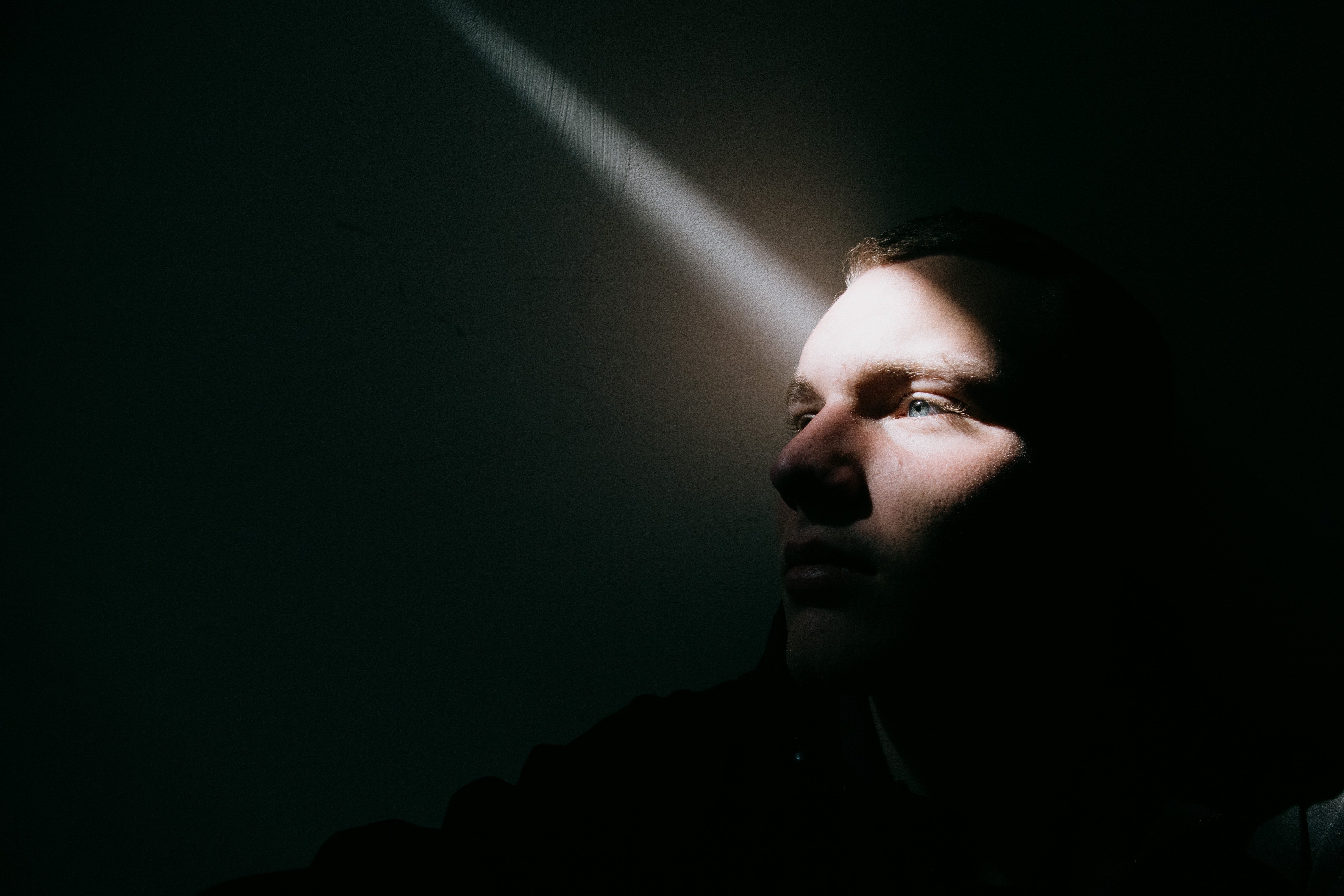 An upset young man sitting on the floor of a dark room with a streak of light seeping in | Source: Pexels