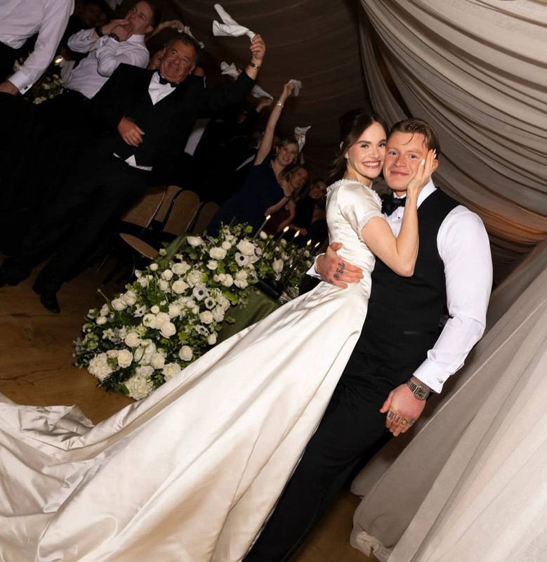 In one of the evening's most heartfelt moments, Holly Ramsay wrapped her arms around Adam Peaty as guests erupted in celebration behind them. The soft draping of her satin gown trailed elegantly across the floor, while white florals and candlelight filled the reception space. With smiles all around, the newlyweds shared a private moment amid the joyful chaos. | Source: Instagram/britishvogue