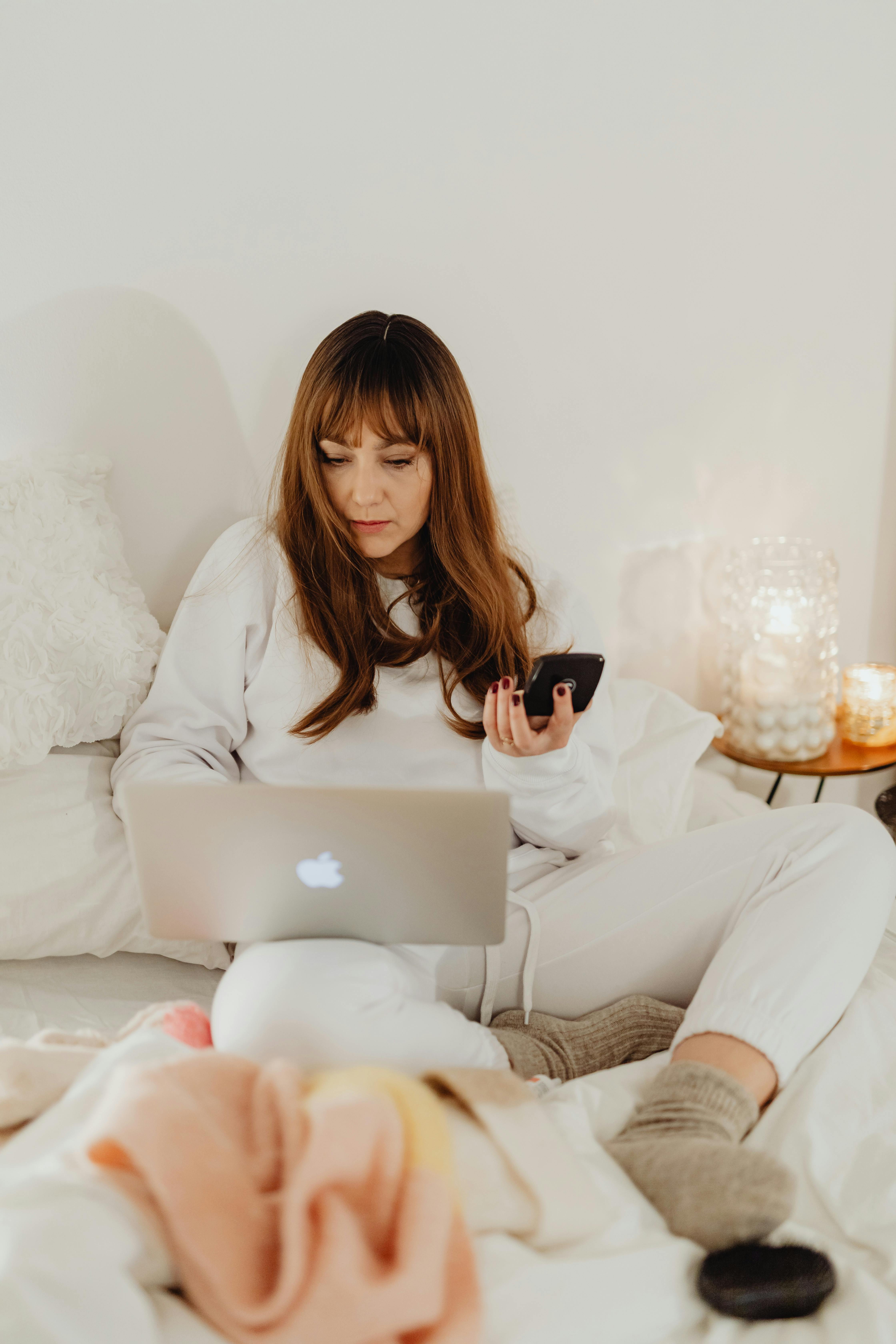 A woman using gadgets on her bed | Source: Pexels