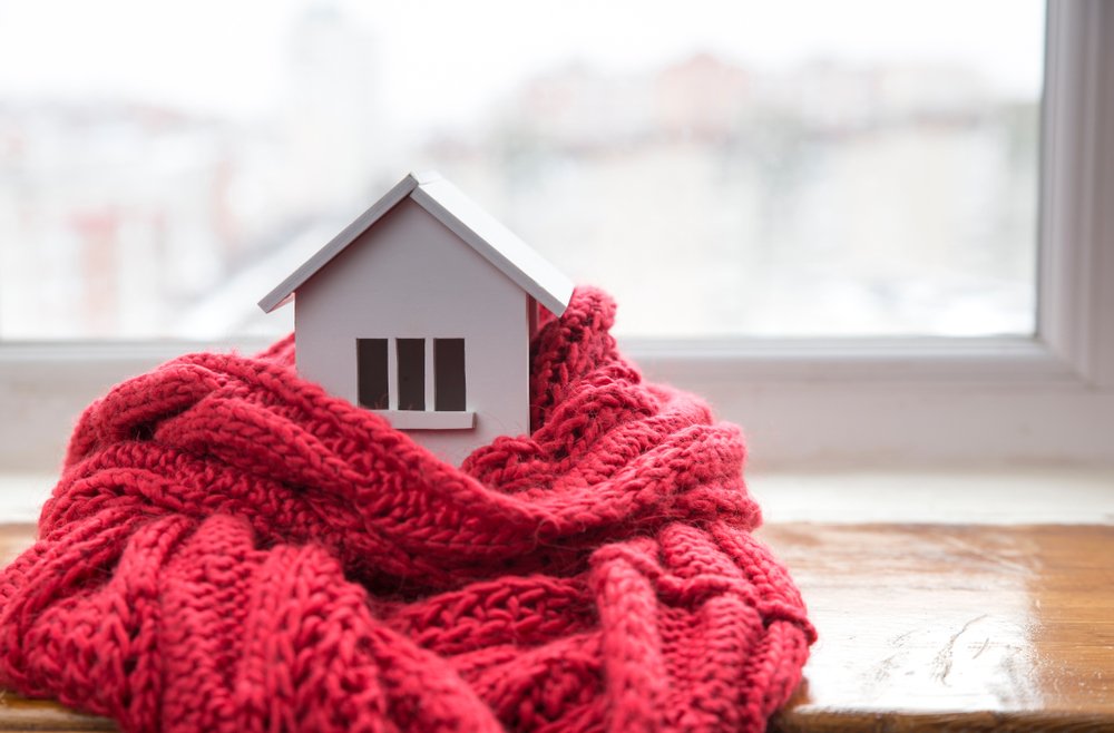 Casa miniatura frente a una ventana cubierta con una bufanda roja.  | Foto: Shutterstock