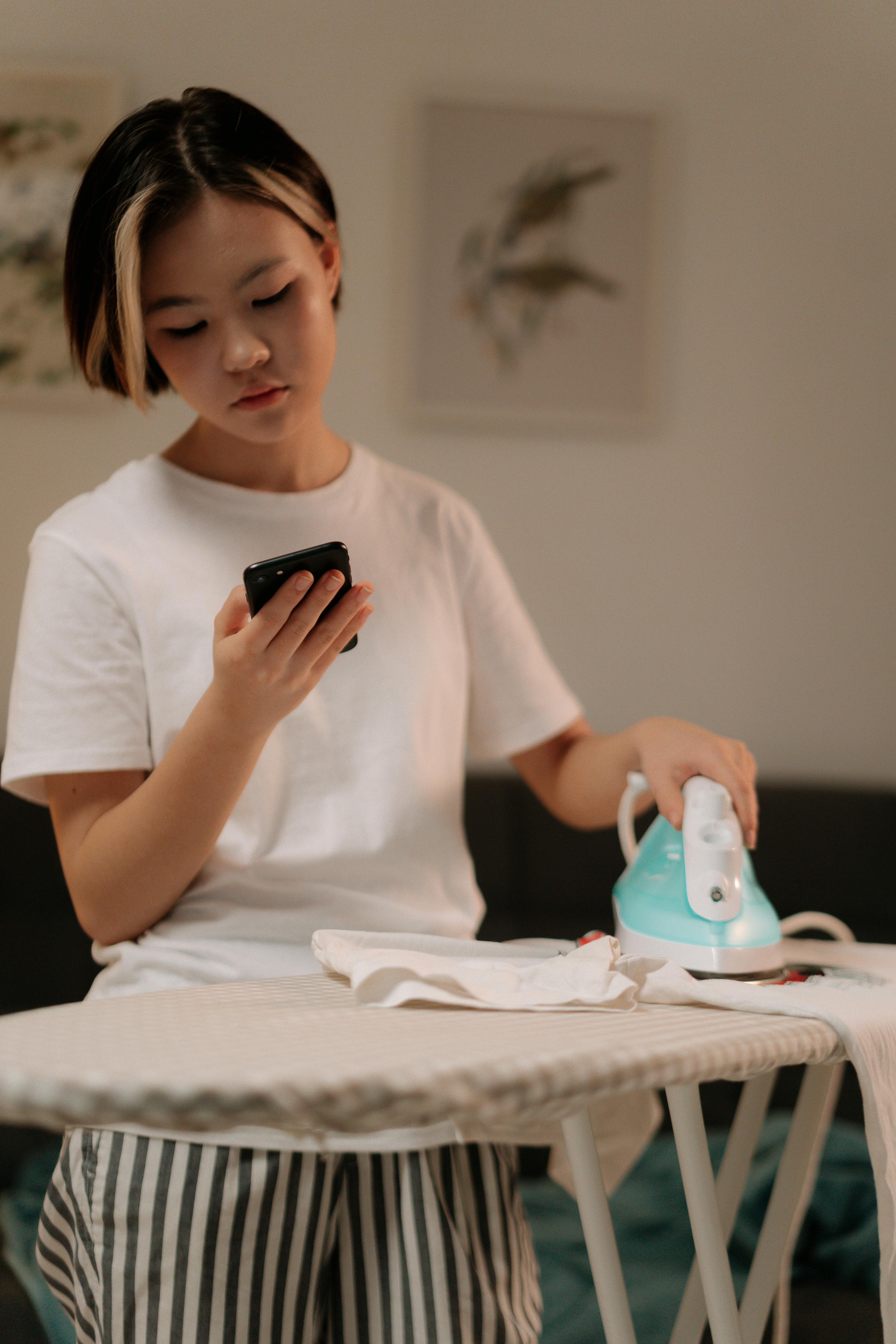 A woman ironing while holding a phone | Source:Pexels