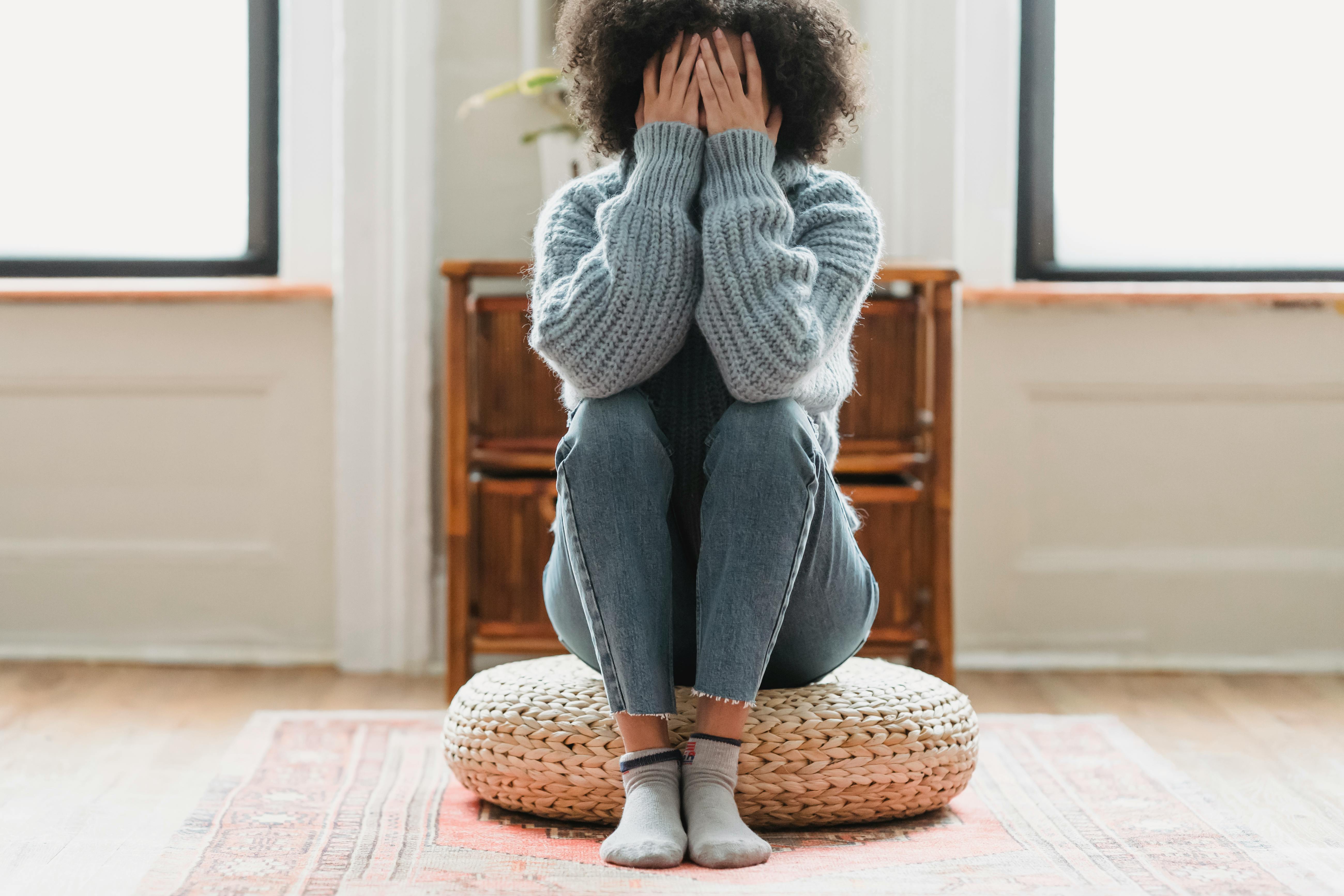 An upset woman sitting on a cushion with her hands covering her face | Source: Pexels