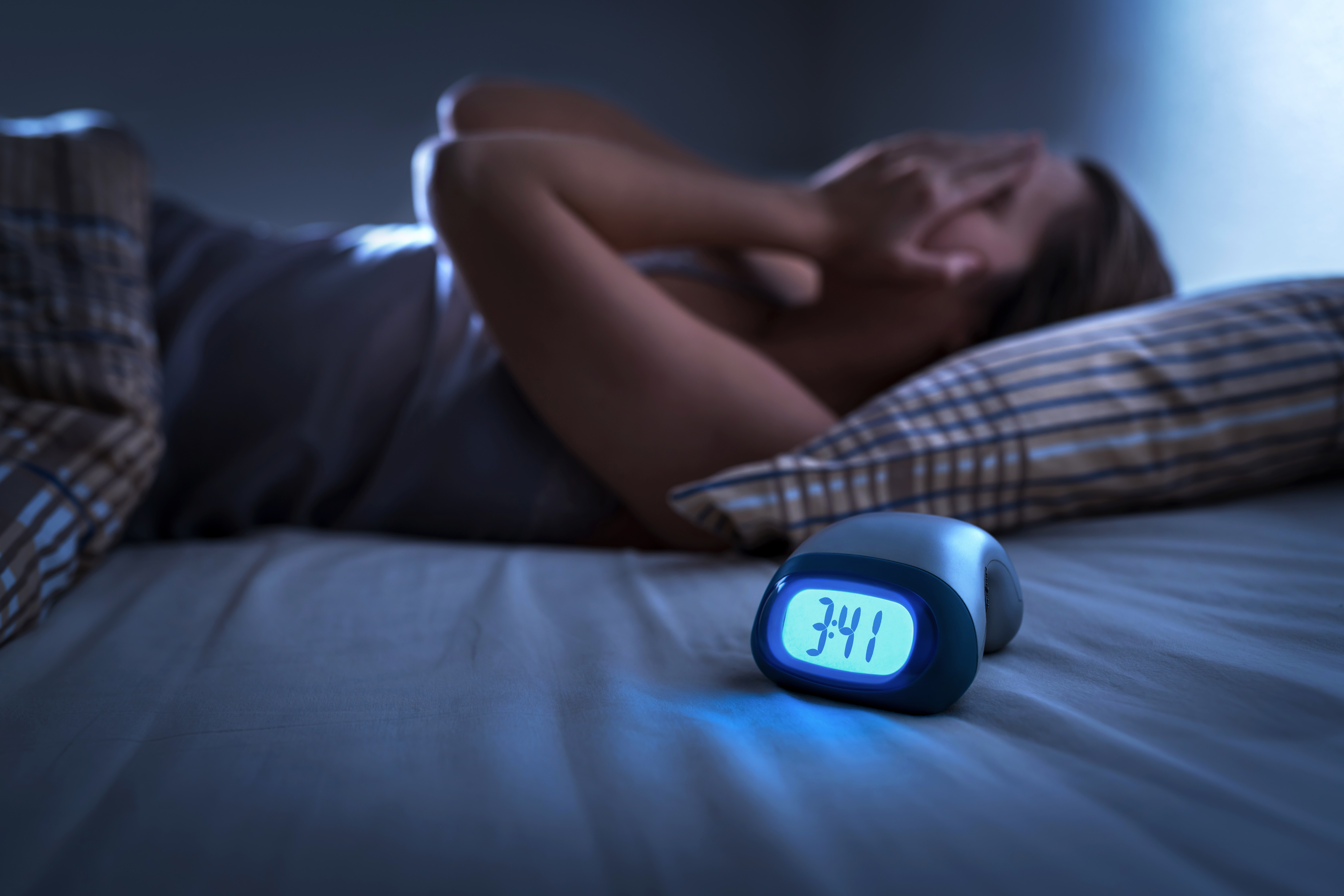 Sleepless woman suffering from insomnia, sleep apnea or stress. Tired and exhausted lady. Headache or migraine. Awake in the middle of the night. Frustrated person with problem. Alarm clock | Source: Getty Images