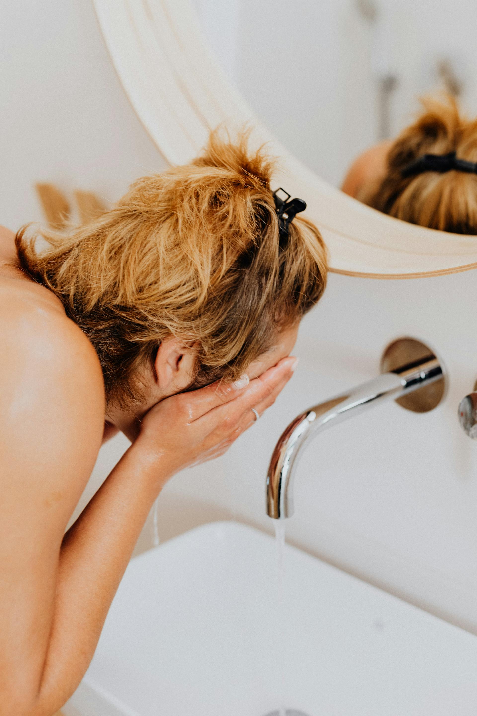 A woman splashing water on her face in the washroom | Source: Pexels