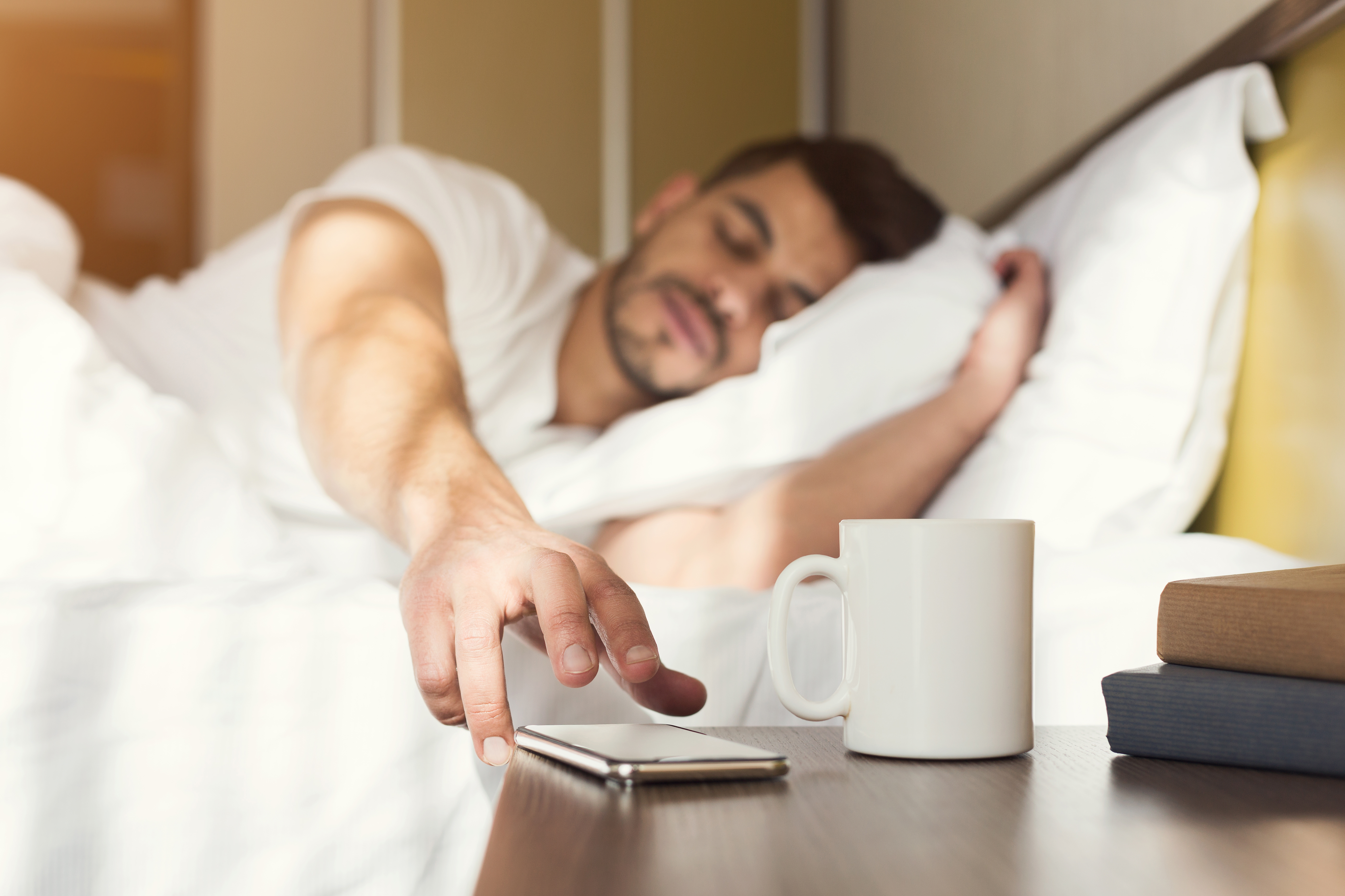 Sleepy guy waking up early after hearing alarm clock signal on smartphone. | Source: Shutterstock
