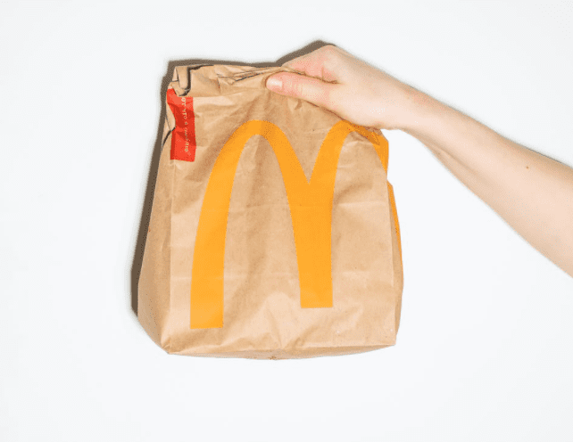 A person holds up a brown takeaway bag from McDonalds | Photo: Pexels/Polina Tankilevitch