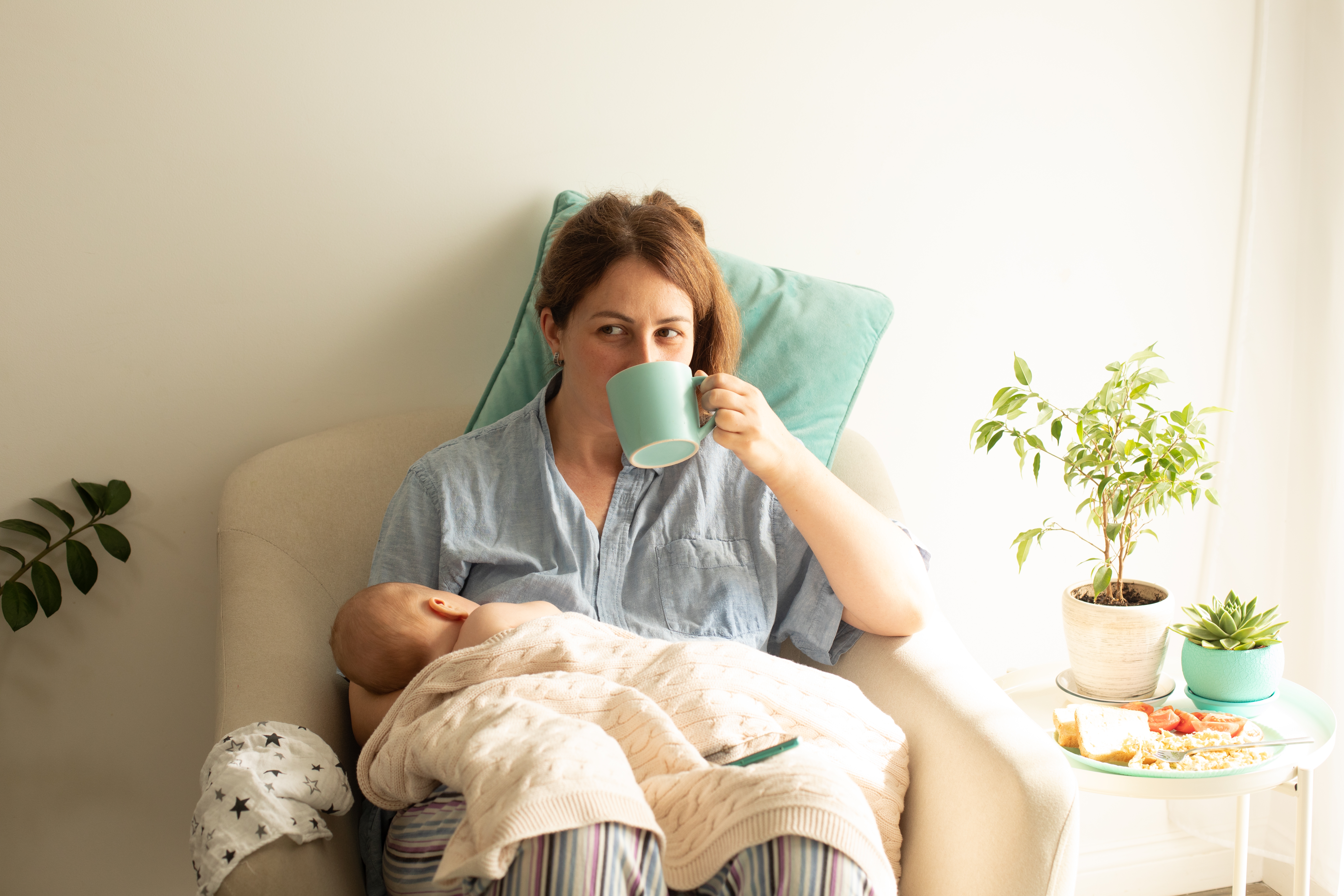 A woman drinking tea while holding her baby | Source: Shutterstock