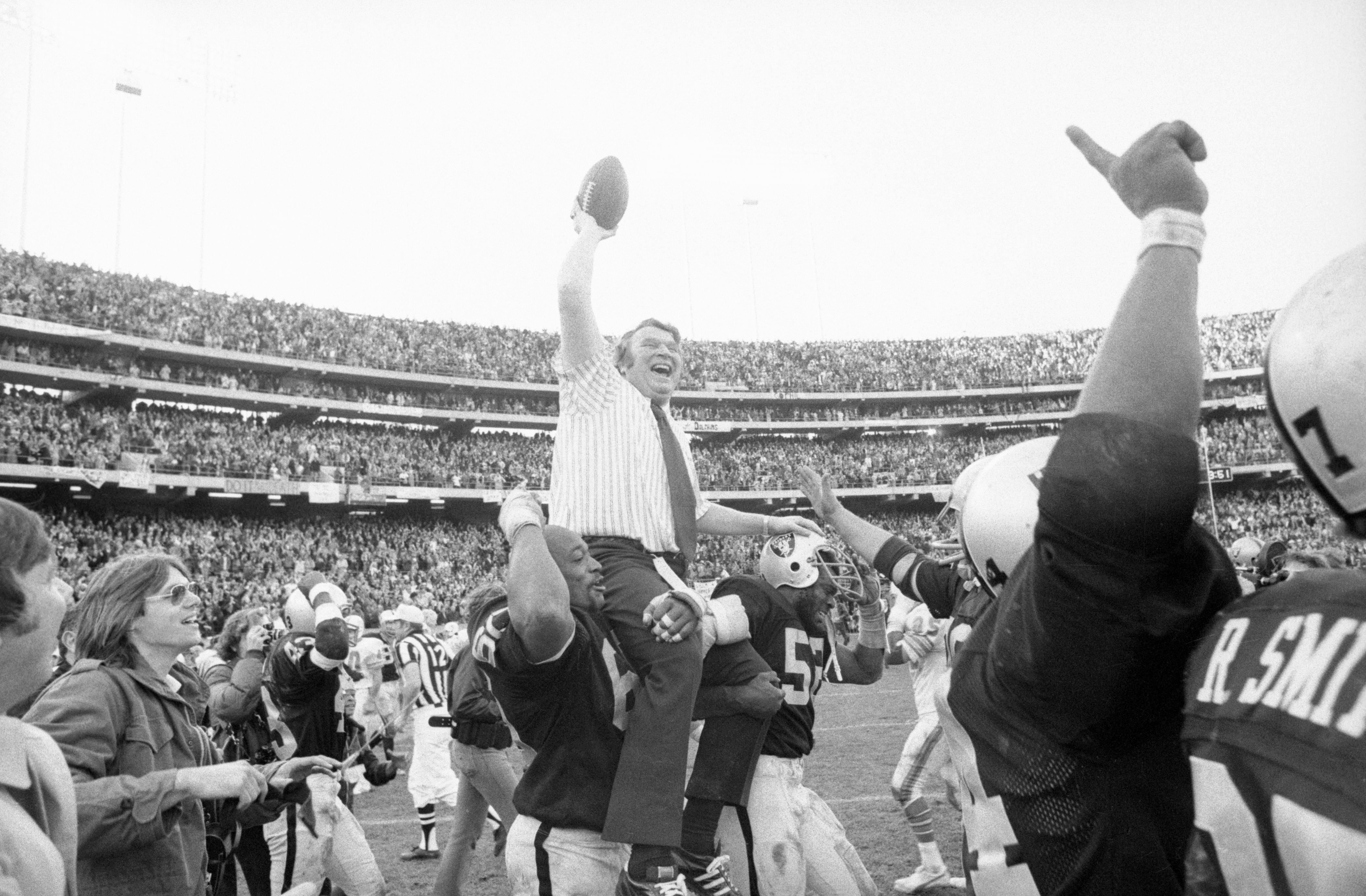 John Madden holds the game ball high in the air as he rides the shoulders of Otis Sistrunk and Gary Weaver  following Oakland Raiders 28-26 victory over Miami in 1974. | Source: Getty Images