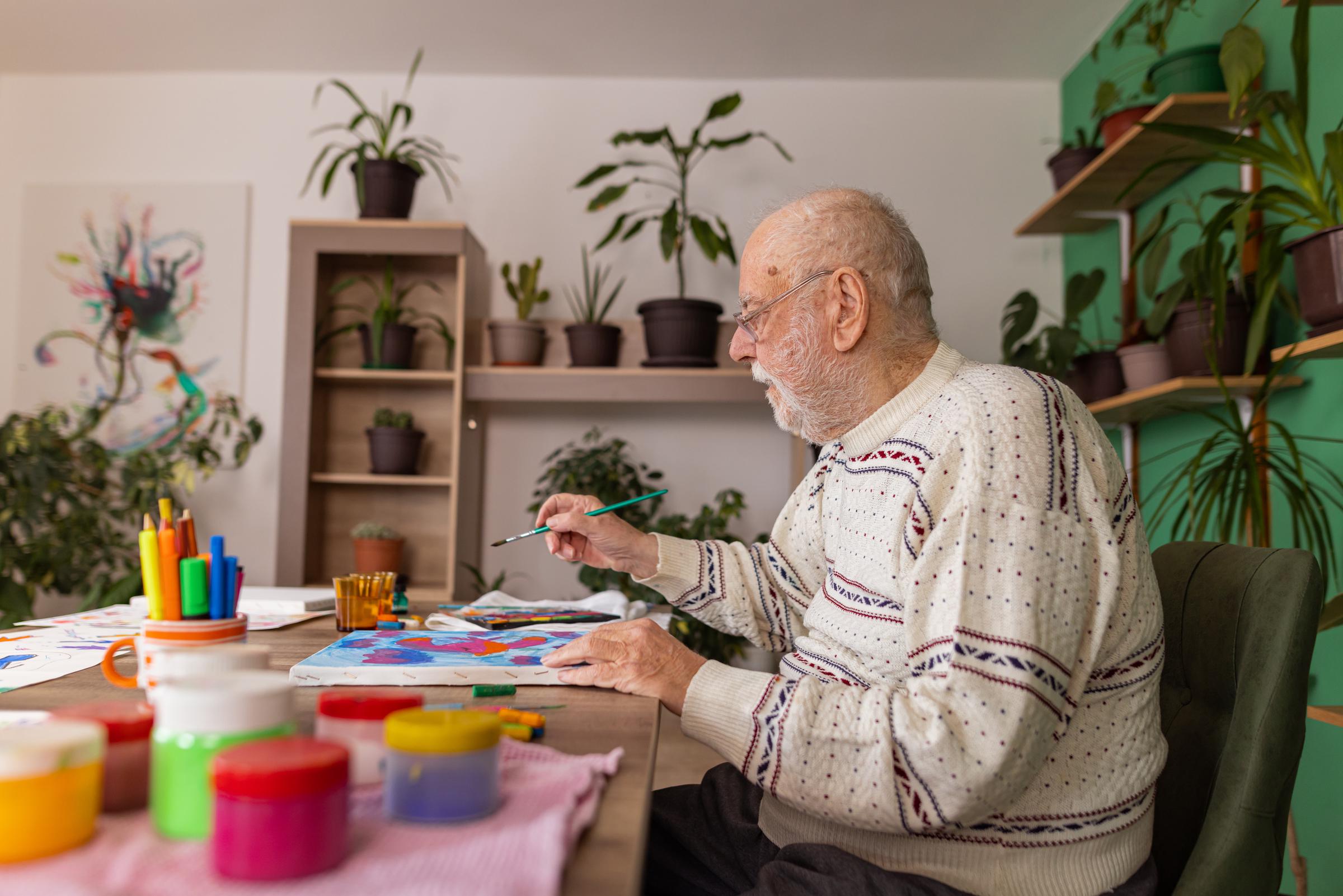 A senior man working on painting in an art class for individuals with dementia | Source: Getty Images