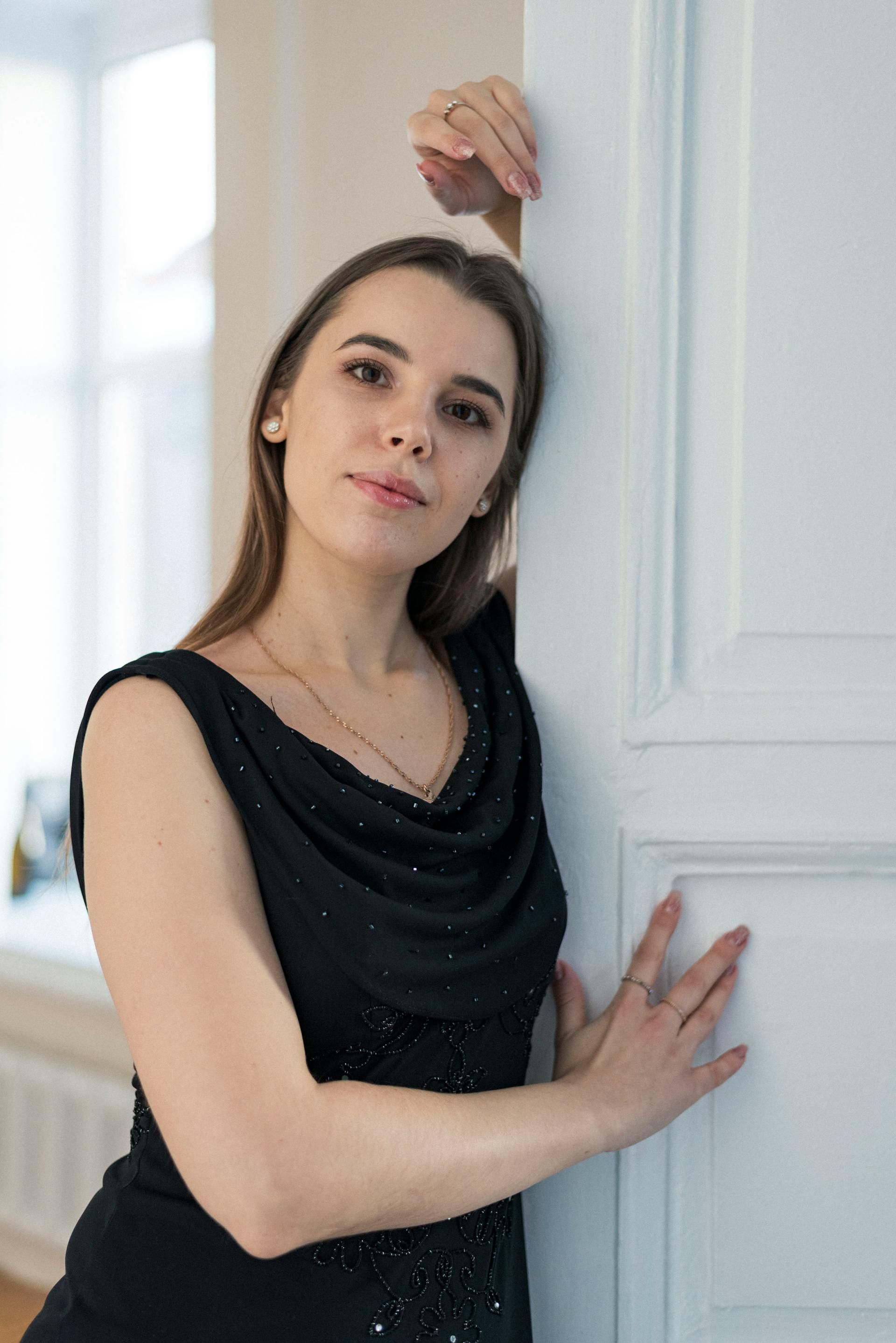 A young woman in a black dress leaning against a door | Source: Pexels