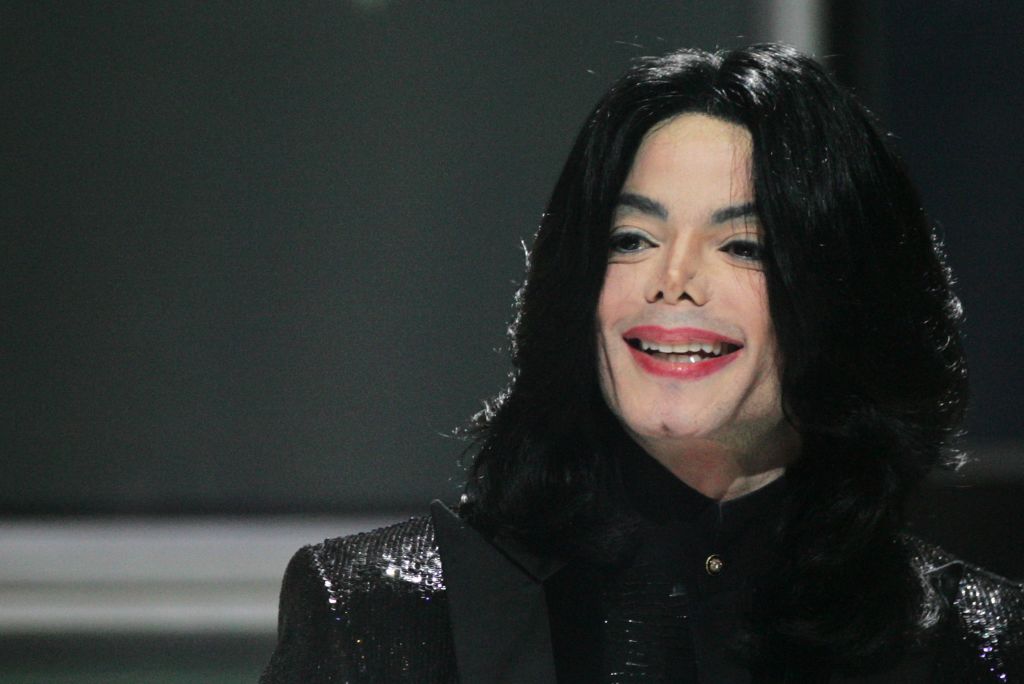 Michael Jackson smiles warmly while dressed in an elegant black sequined jacket over a black shirt. | Source: Getty Images