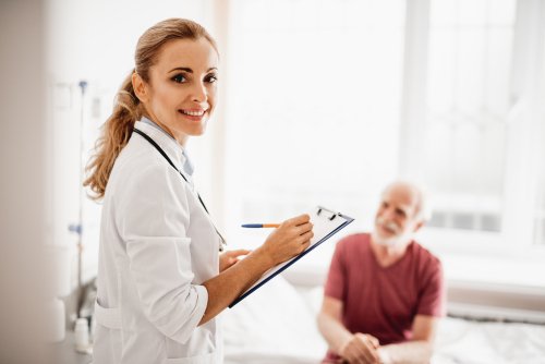 Lady in white lab coat holding clipboard and an elderly man sitting on the bed. | Source: Shutterstock