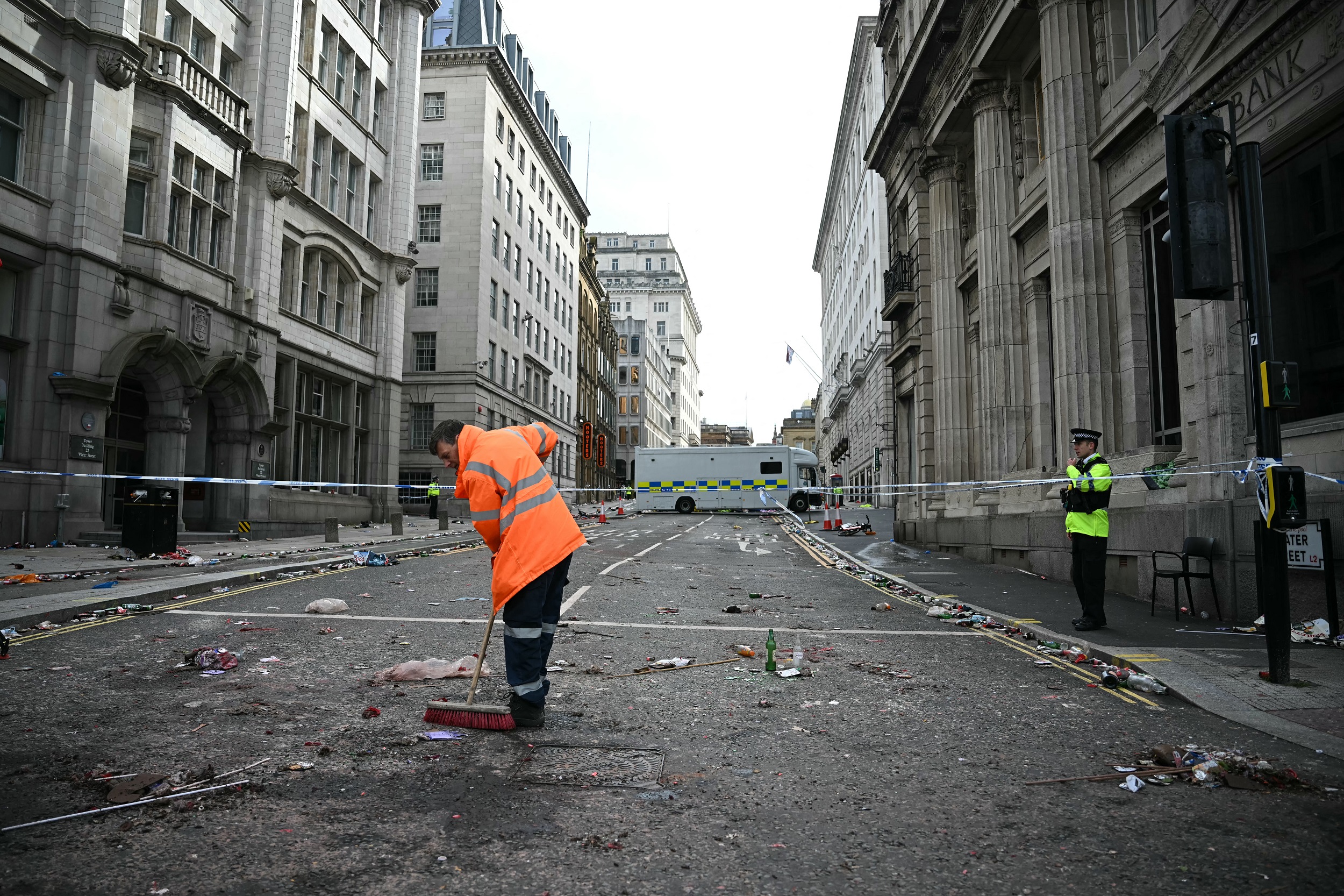 A worker cleans debris as a police officer stands at a cordon on Water Street in Liverpool, north-west England on May 27, 2025, after a car ploughed into crowds watching Liverpool's Premier League trophy parade on May 26 | Source: Getty Images