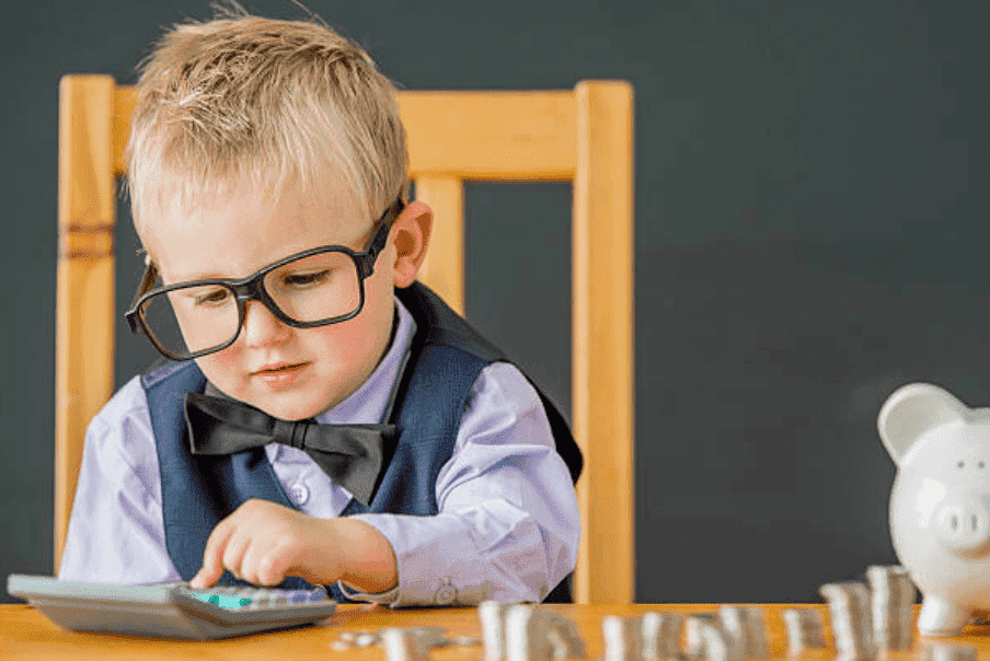 Little boy wearing glasses and a bow tie count's coins for his piggy bank using a calculator | Source: Getty Images