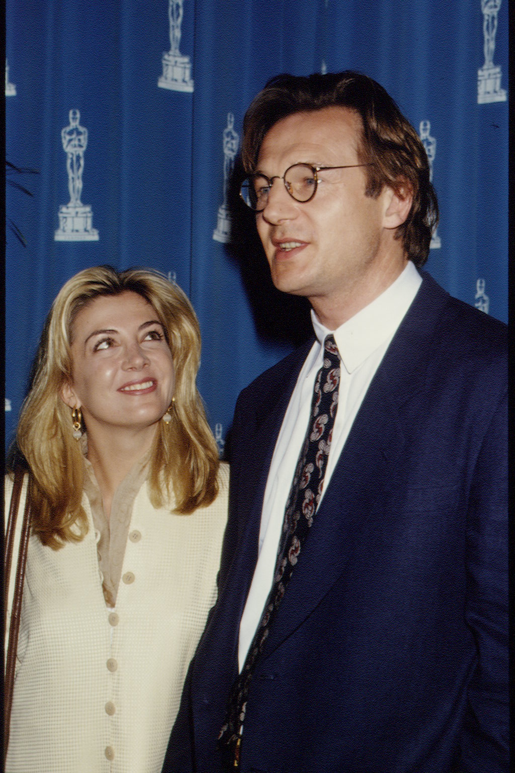 Natasha Richardson looks up at Liam Neeson with a smile during Oscar Nominees Night on March 8, 1994. The couple stands in front of a backdrop featuring the Academy Awards logo while attending the pre-Oscars event together.