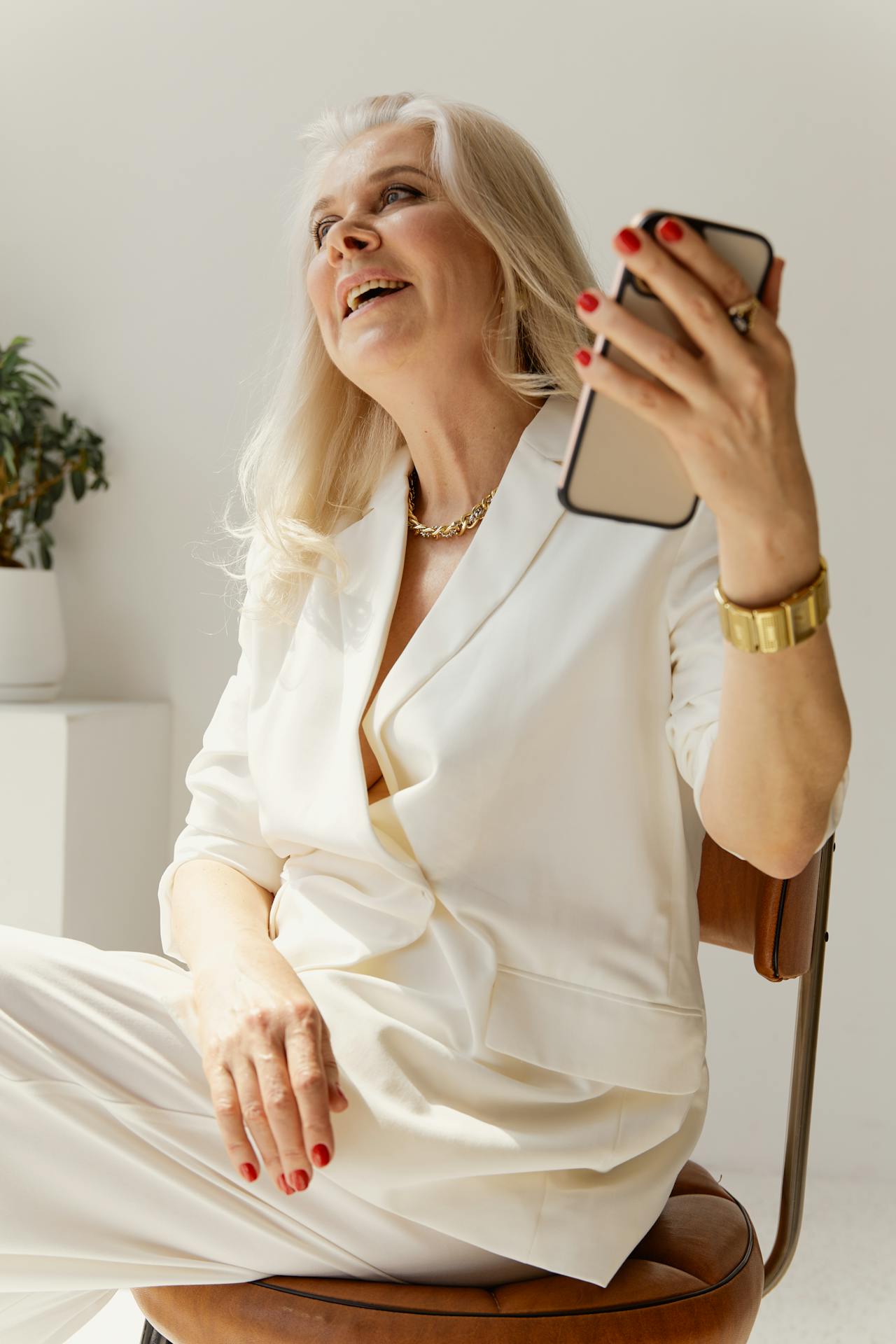 A smiling senior woman holding her phone while sitting on a chair | Source: Pexels