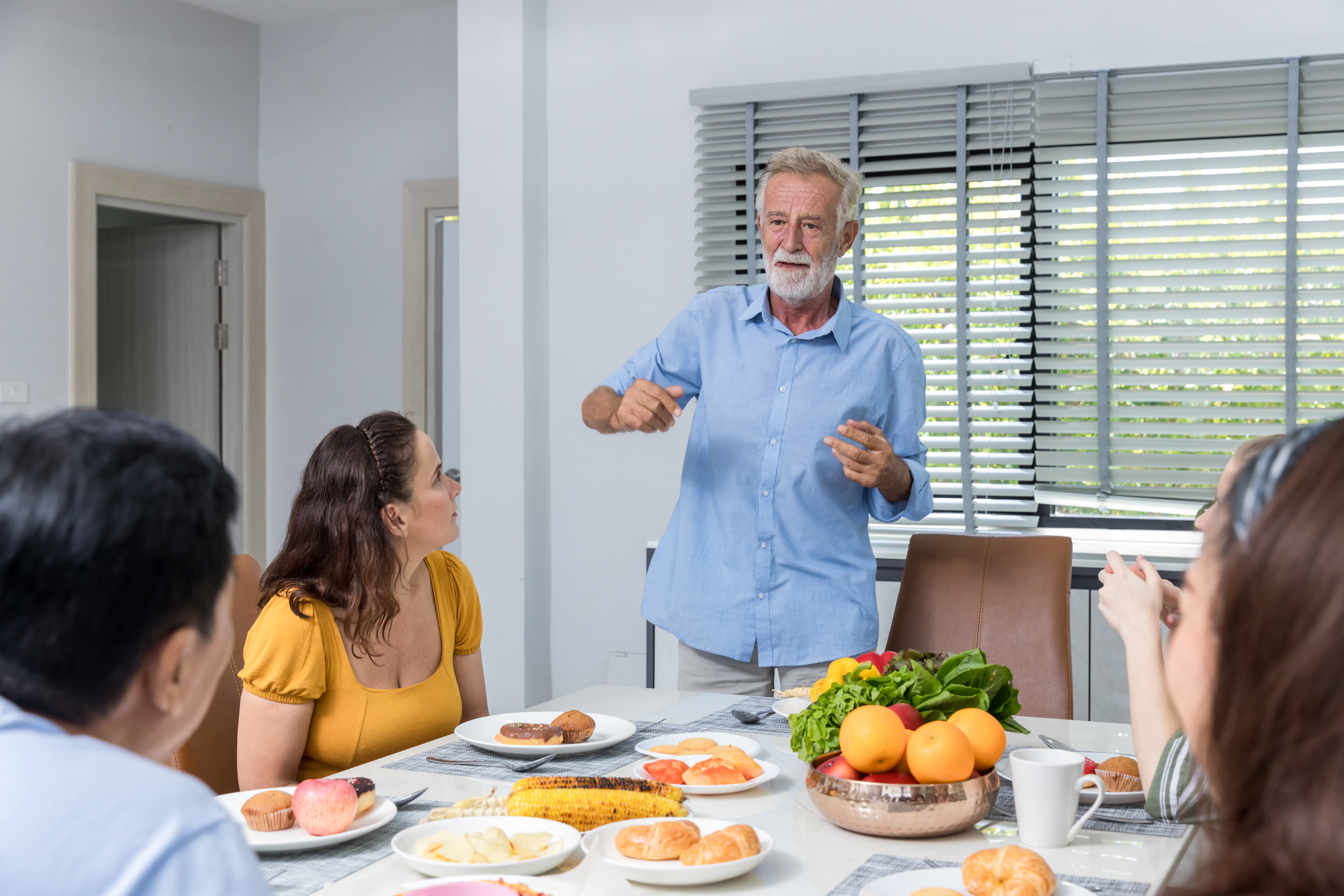 An elderly man speaking to his family members at the table | Source: Shutterstock