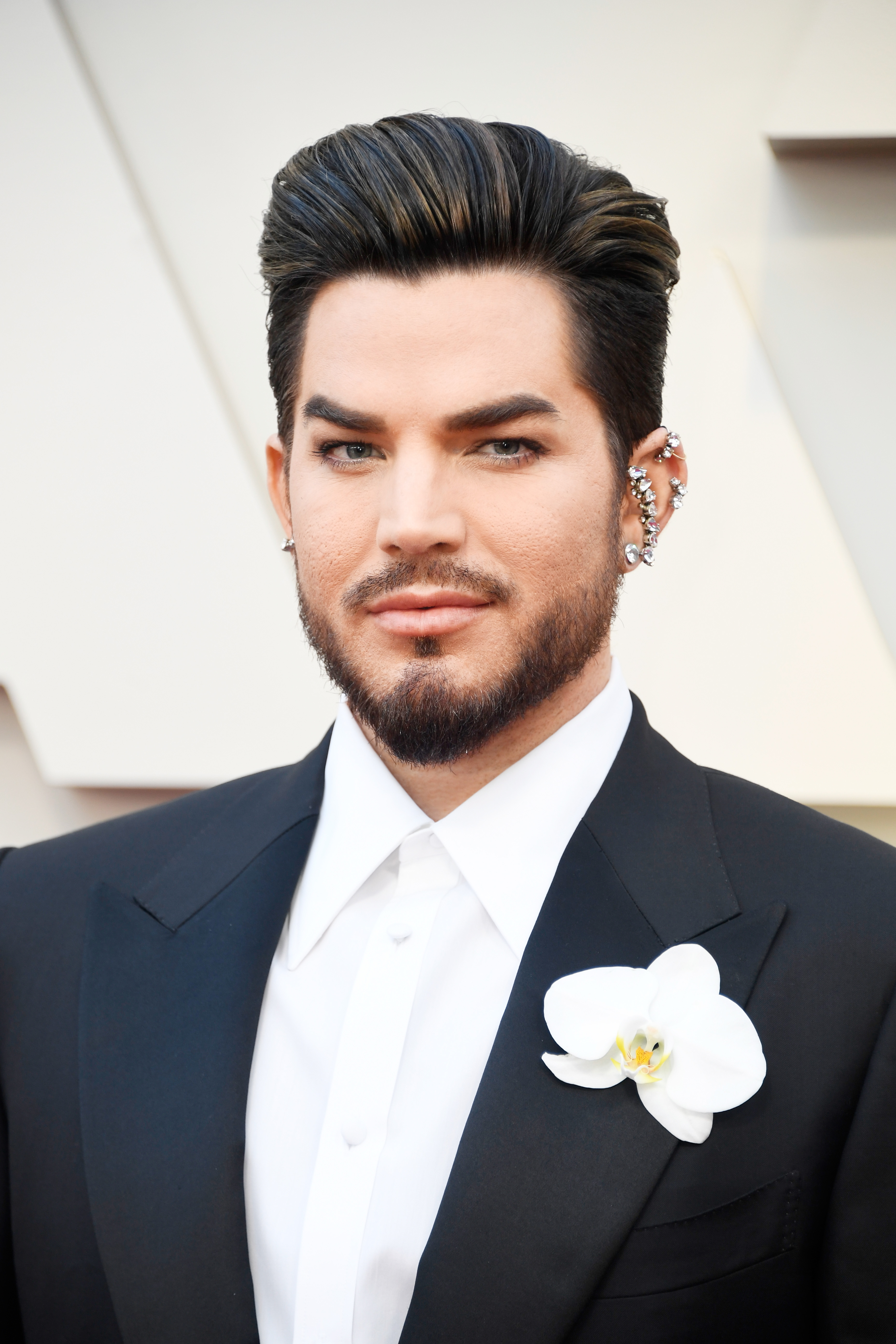 On February 24, 2019, Adam Lambert attends the 91st Academy Awards in Hollywood, California. Dressed in a sharp black suit with a white orchid boutonnière and diamond ear cuff, he delivers an elegant, modern twist on classic red carpet formality.