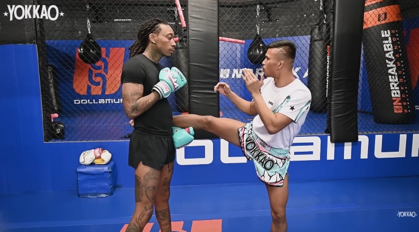 Superlek Kiatmoo9 demonstrates kicking technique as Wiz Khalifa follows along during their training session. | Source: YouTube/YOKKAO