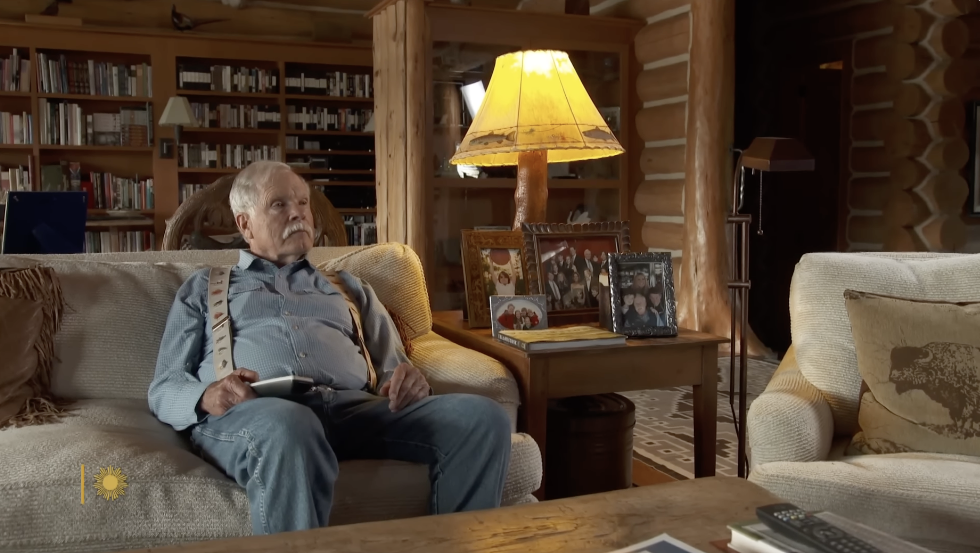 Ted Turner relaxes inside his cozy lodge-style living room, where family photographs and rustic furnishings reflect his deeply personal connection to ranch life. | Source: YouTube/CBS Sunday Morning