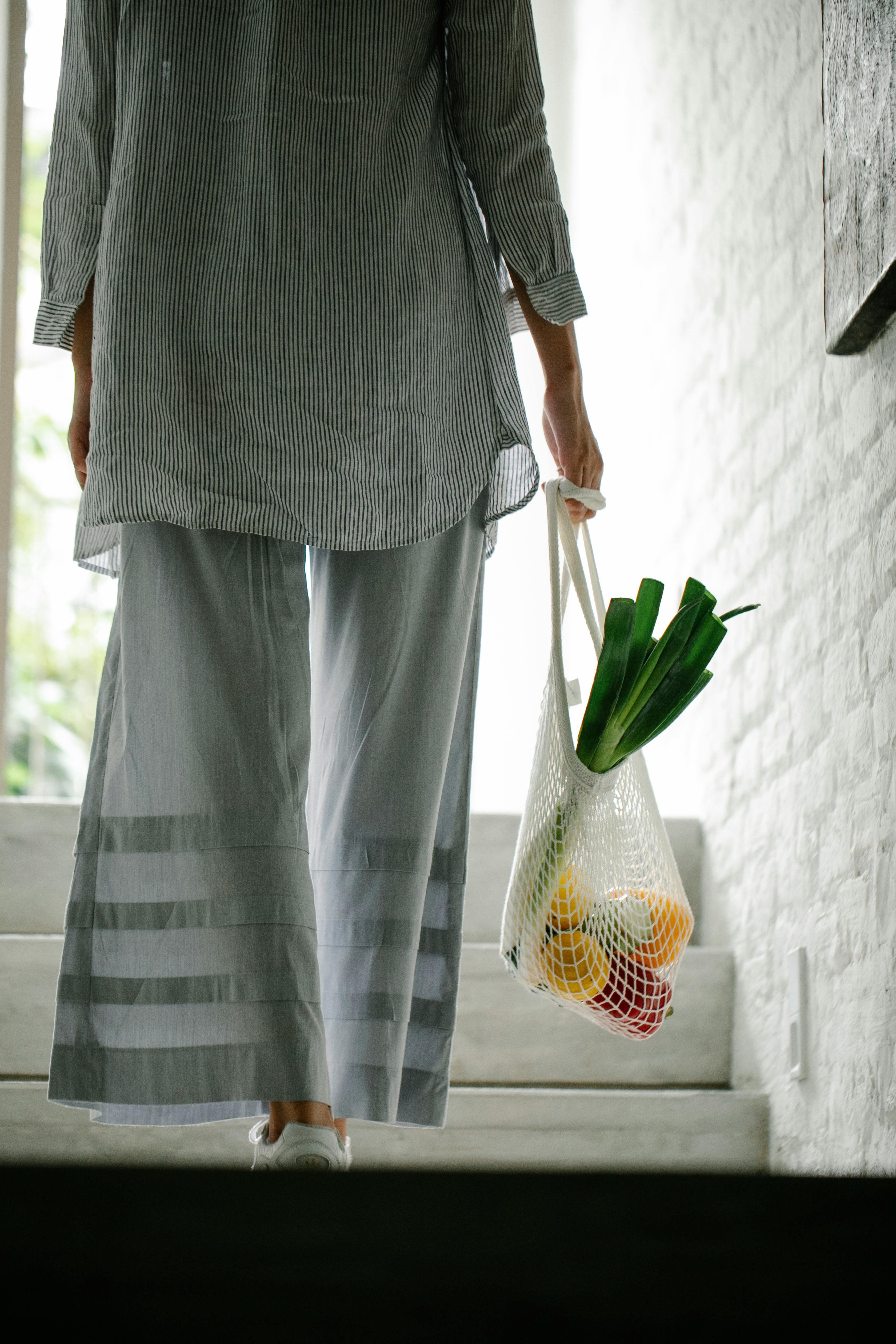 A woman carrying vegetables in a bag on a house staircase | Source: Pexels