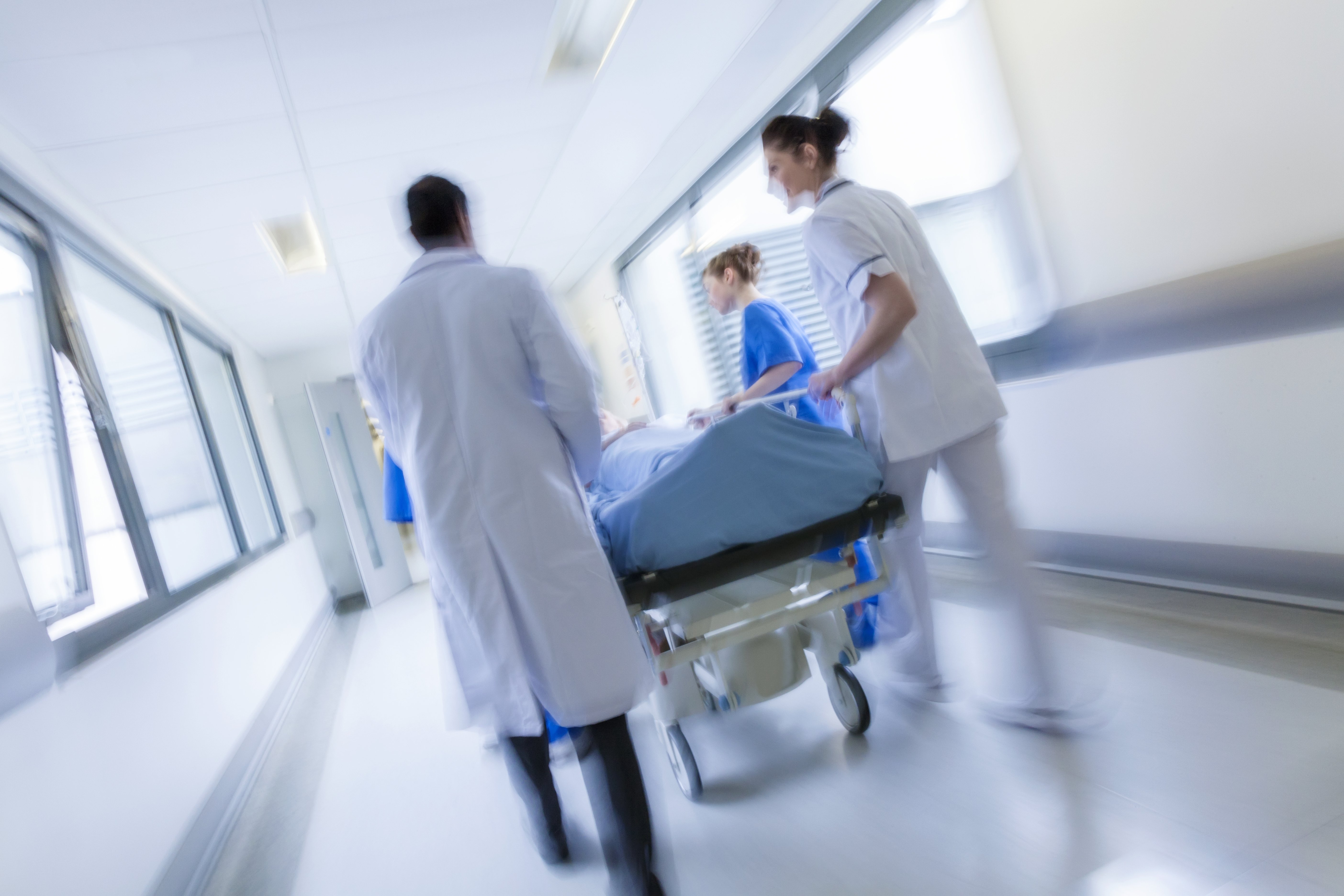 Ein bewegungsunscharfes Foto eines Patienten auf einer Trage, der von Ärzten und Krankenschwestern durch einen Krankenhauskorridor in eine Notaufnahme geschoben wird | Quelle: Shutterstock