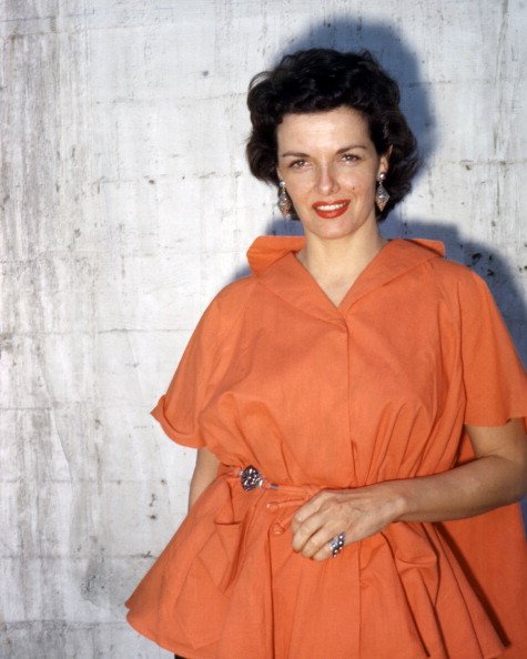 Photo of Jane Russell wearing an orange dress, with large drop earrings, in a studio portrait, against a white background, circa 1955. | Photo: Getty Images
