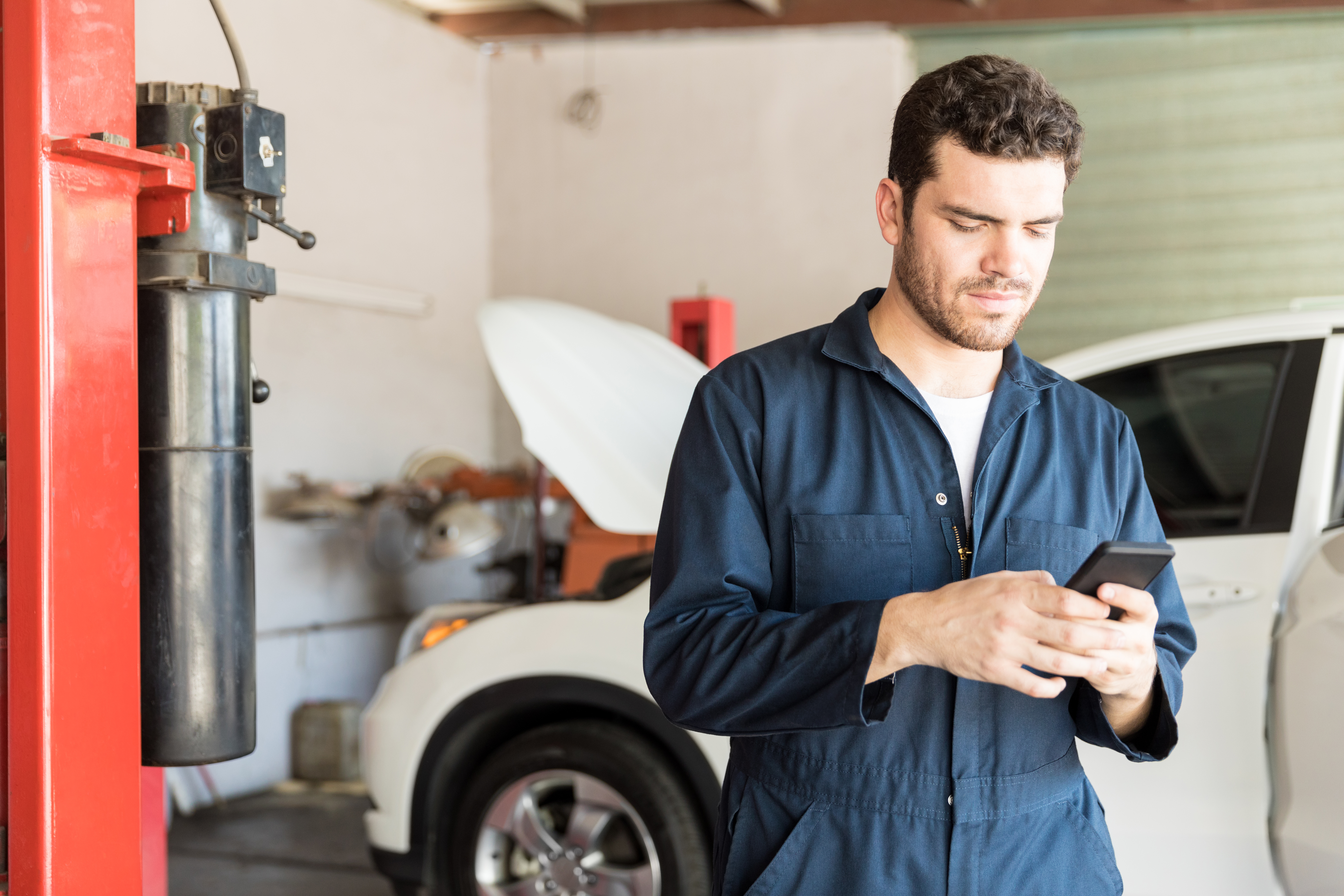 Mid adult maintenance worker using mobile phone in auto repair shop | Source: Shutterstock