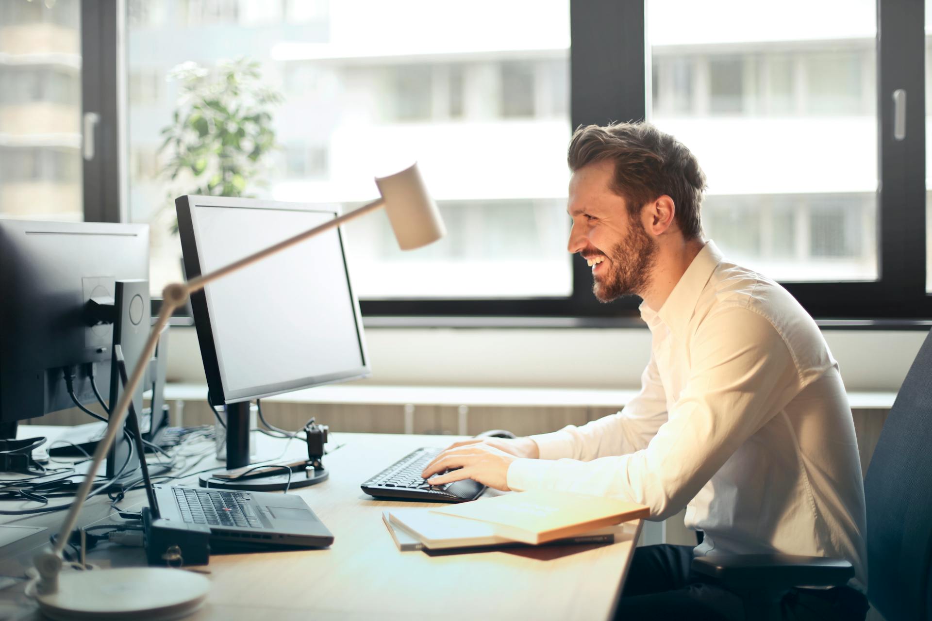 A man smiling while staring at a computer screen and typing on the keyboard | Source: Pexels