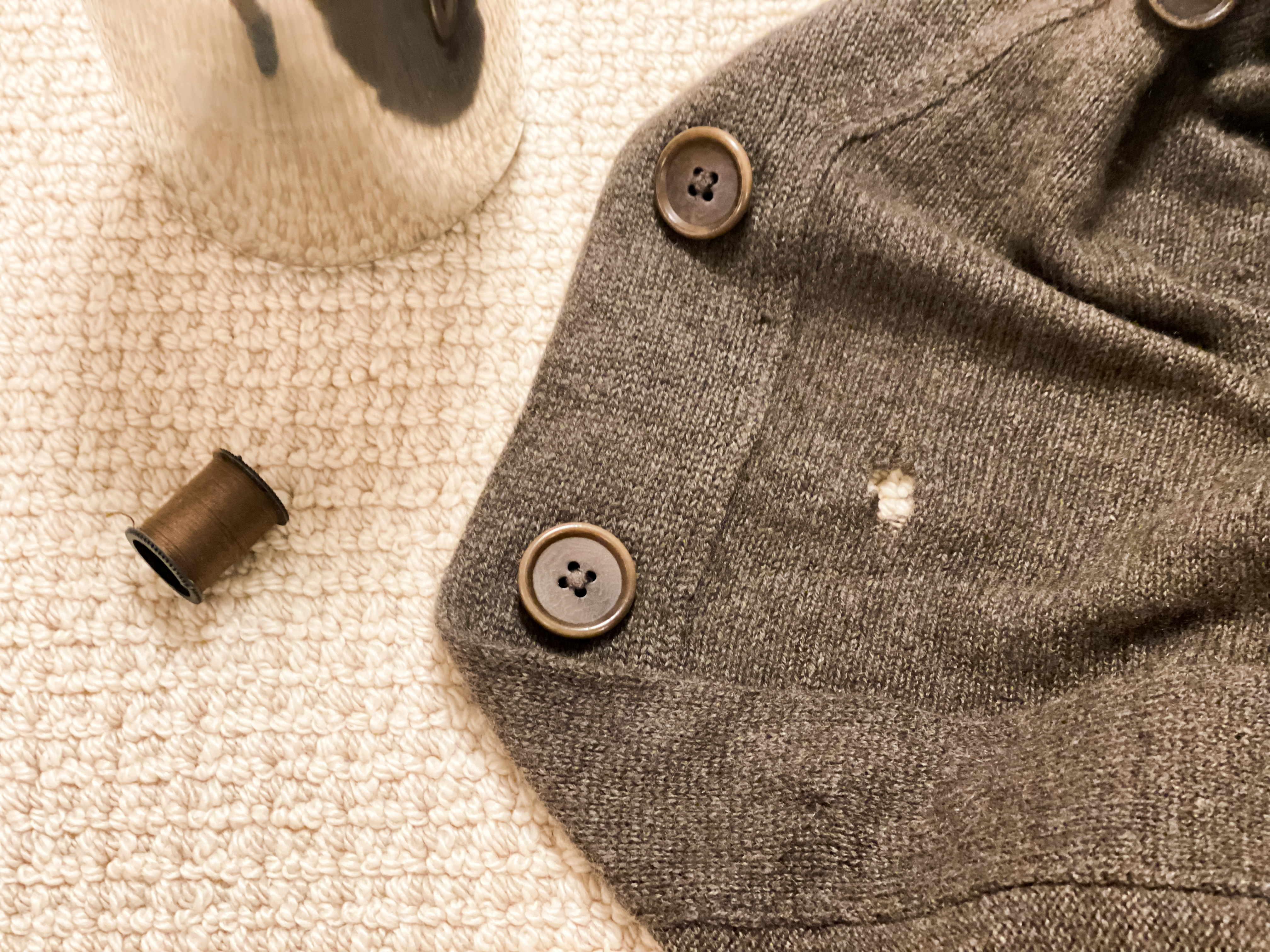 A cashmere cardigan with a small hole and a small roll of cotton thread | Source: Getty Images