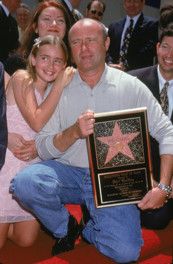 Le chanteur/musicien britannique Phil Collins pose avec ses filles, Lily et Joely (derrière Lily), en s'agenouillant près de son étoile sur le Hollywood Walk of Fame, en Californie, le 16 juin 1999. | Photo : Getty Images