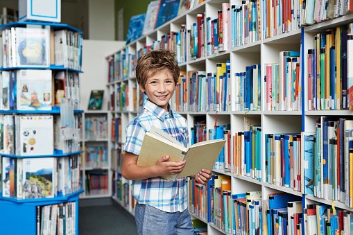 Photo  of a cute boy standing in a school library, holding a book | Photo: Getty Images