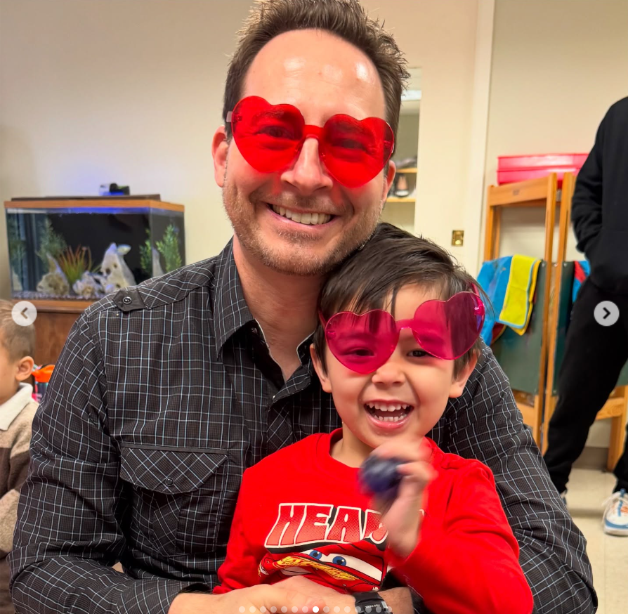 Matthew Mitchell and his son share a playful moment while wearing matching oversized red heart-shaped glasses indoors. | Source: Instagram/thy_travelers