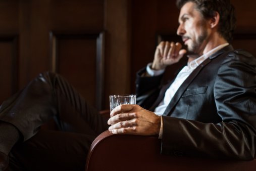 Foto eines reifen Mannes, der in einer dunklen Bar sitzt und ein Whiskeyglas hält | Quelle: Getty Images