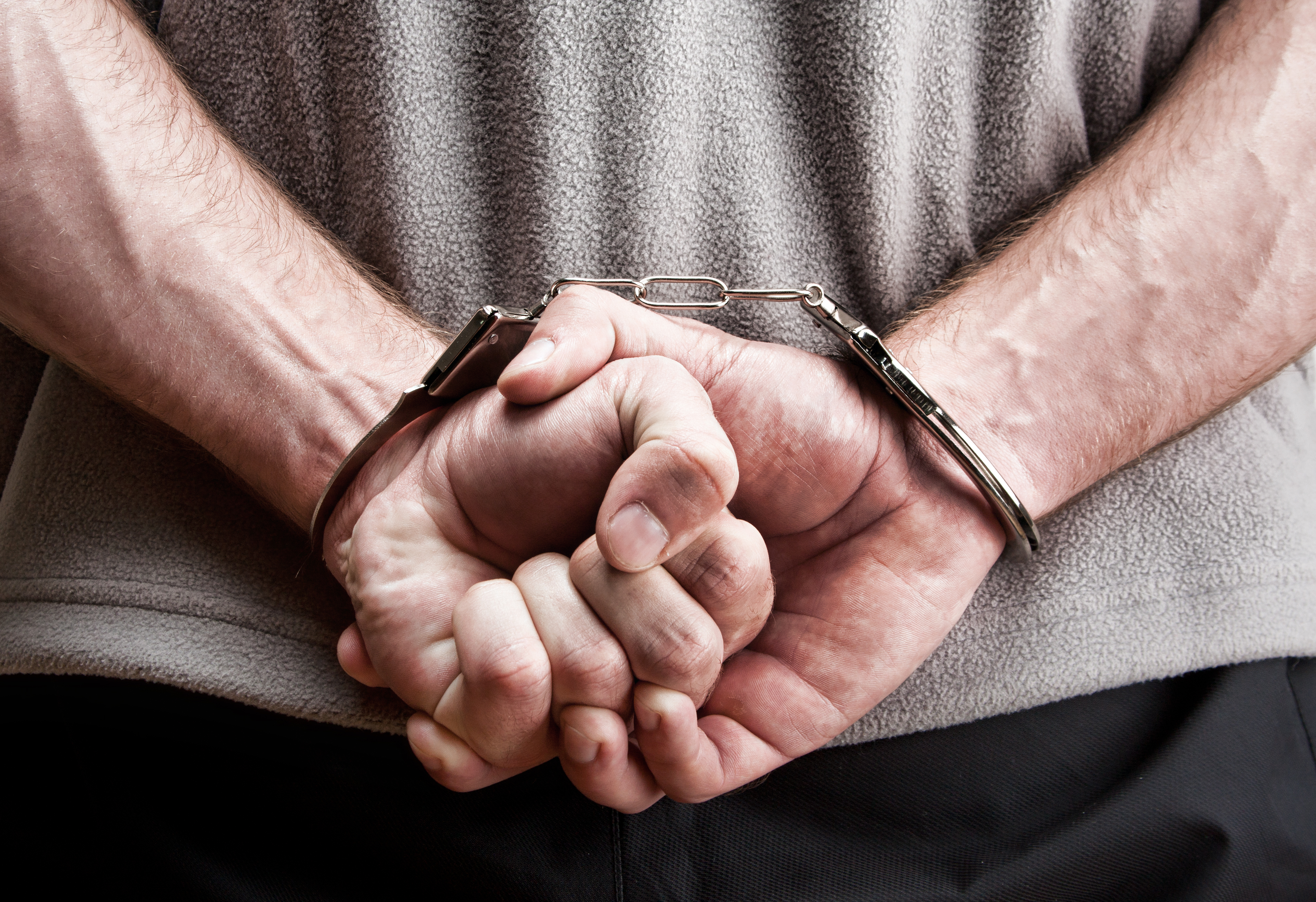 Criminal hands locked in handcuffs. | Source: Shutterstock