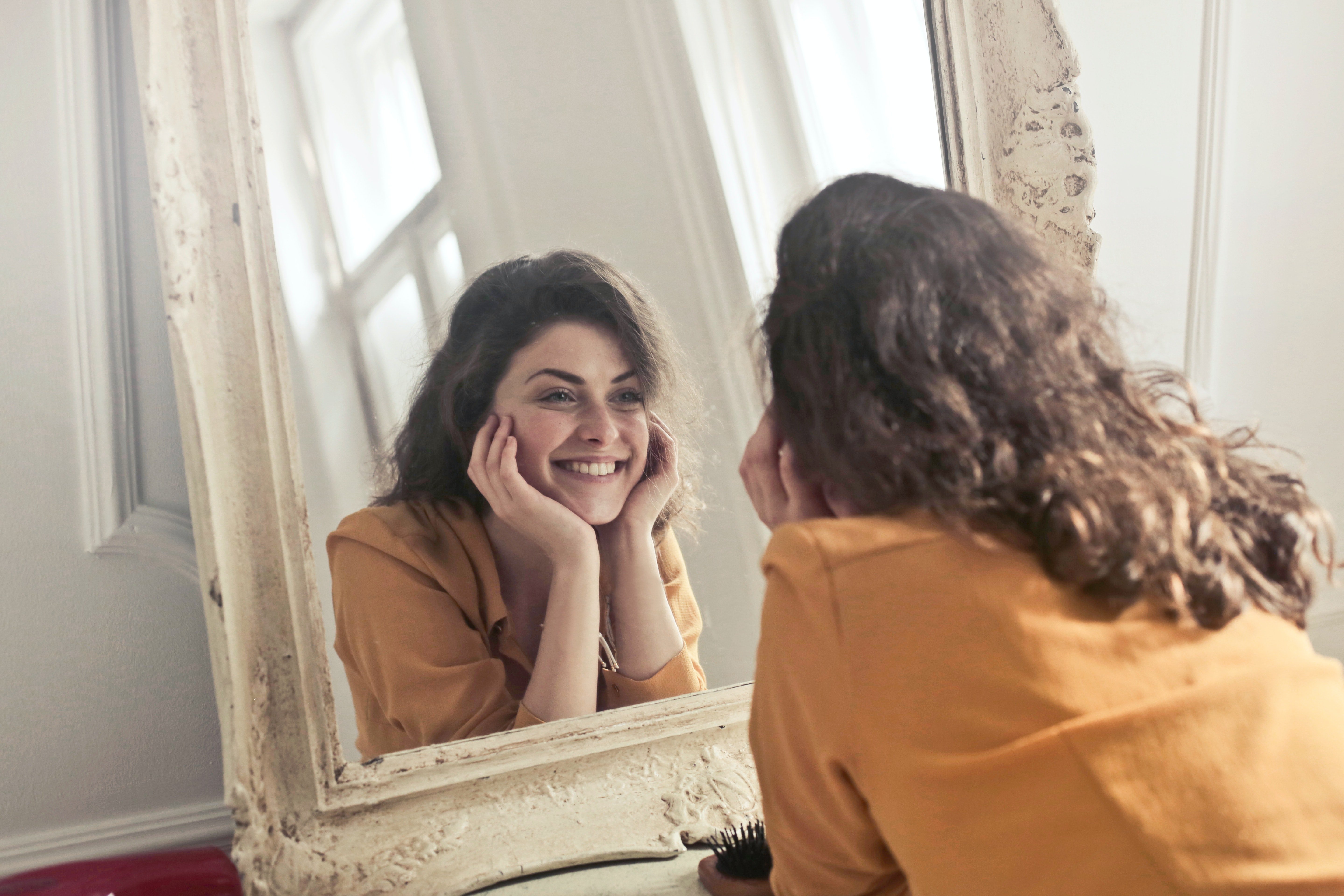 Mujer sonriendo frente al espejo. | Foto: Pexels