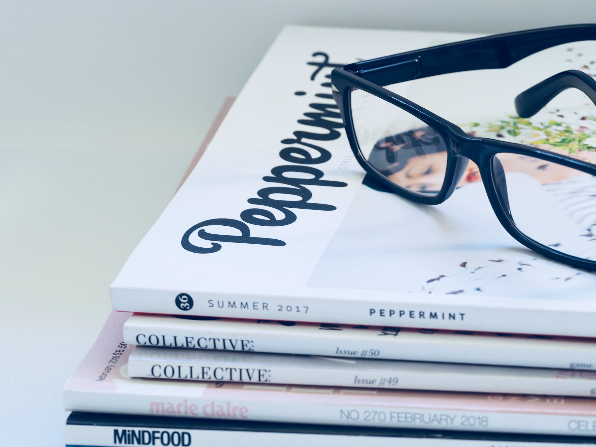 A pair of black sunglasses lying on a stack of magazines | Source: Pexels