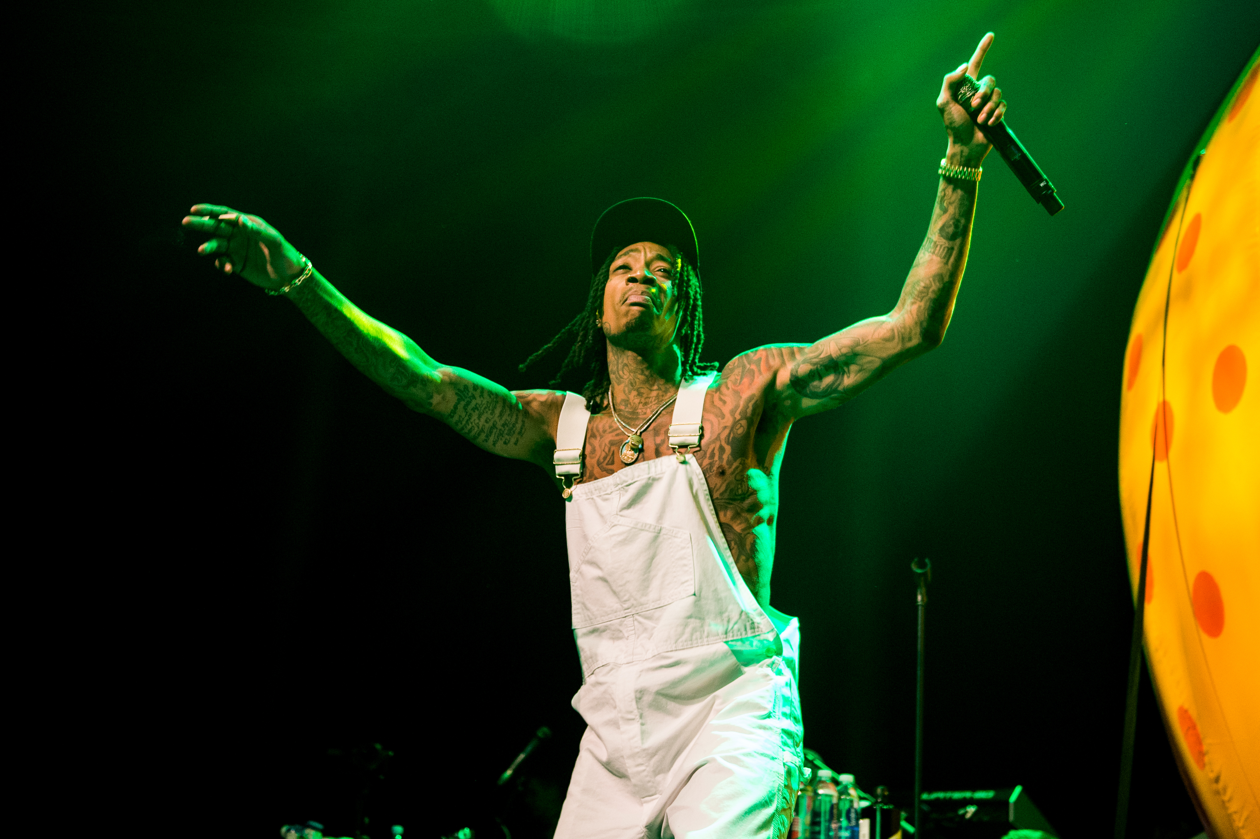 Wiz Khalifa raises his arms to the crowd while performing at The Roundhouse in London, England, on July 1, 2018. Even with much of his physique covered by white overalls, his noticeably broader arms and upper body reflected the physical transformation he achieved through years of dedicated MMA training.
