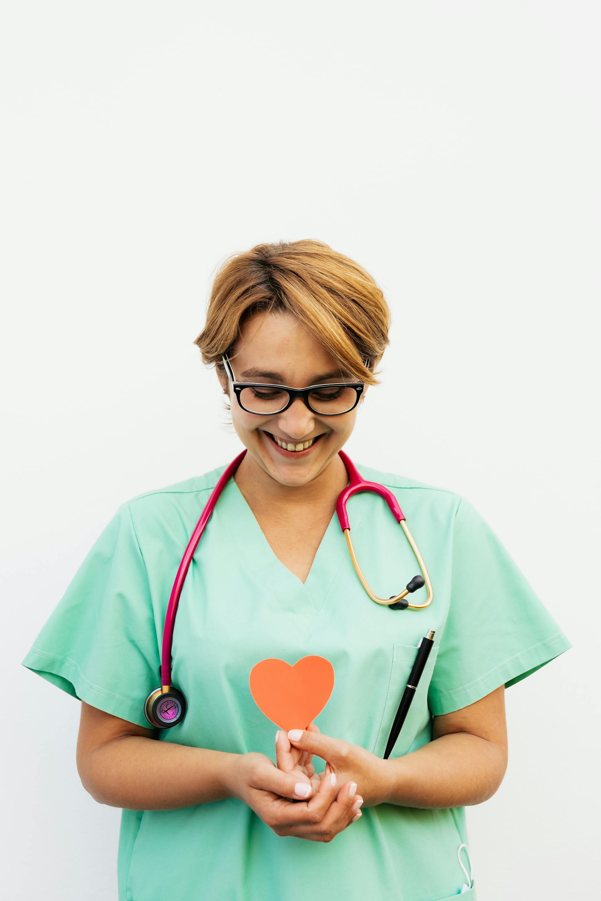 A smiling nurse holding a red paper heart | Source: Pexels