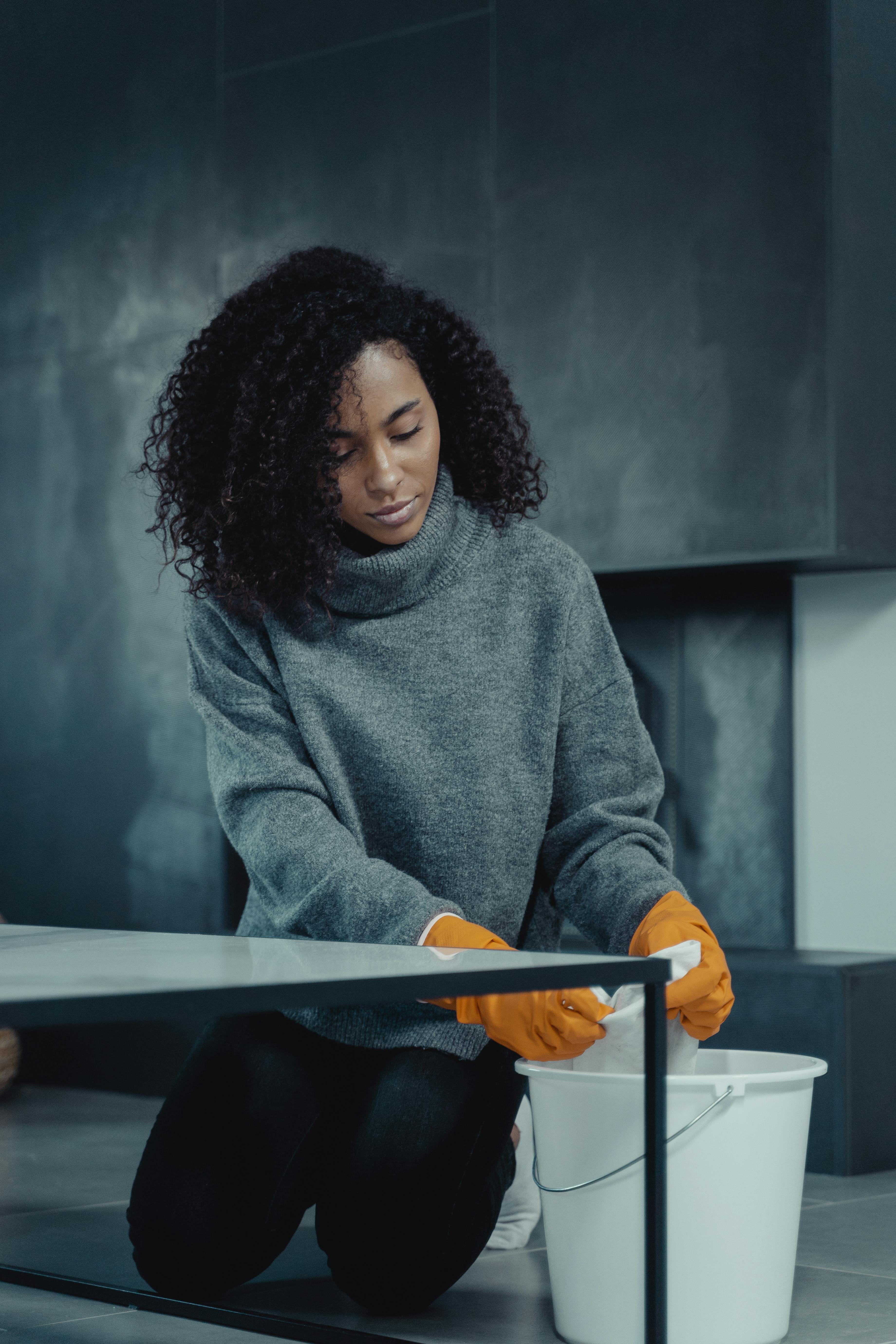 A woman wearing gloves wipes down a table, highlighting the importance of disinfecting everyday surfaces. | Source: Pexels