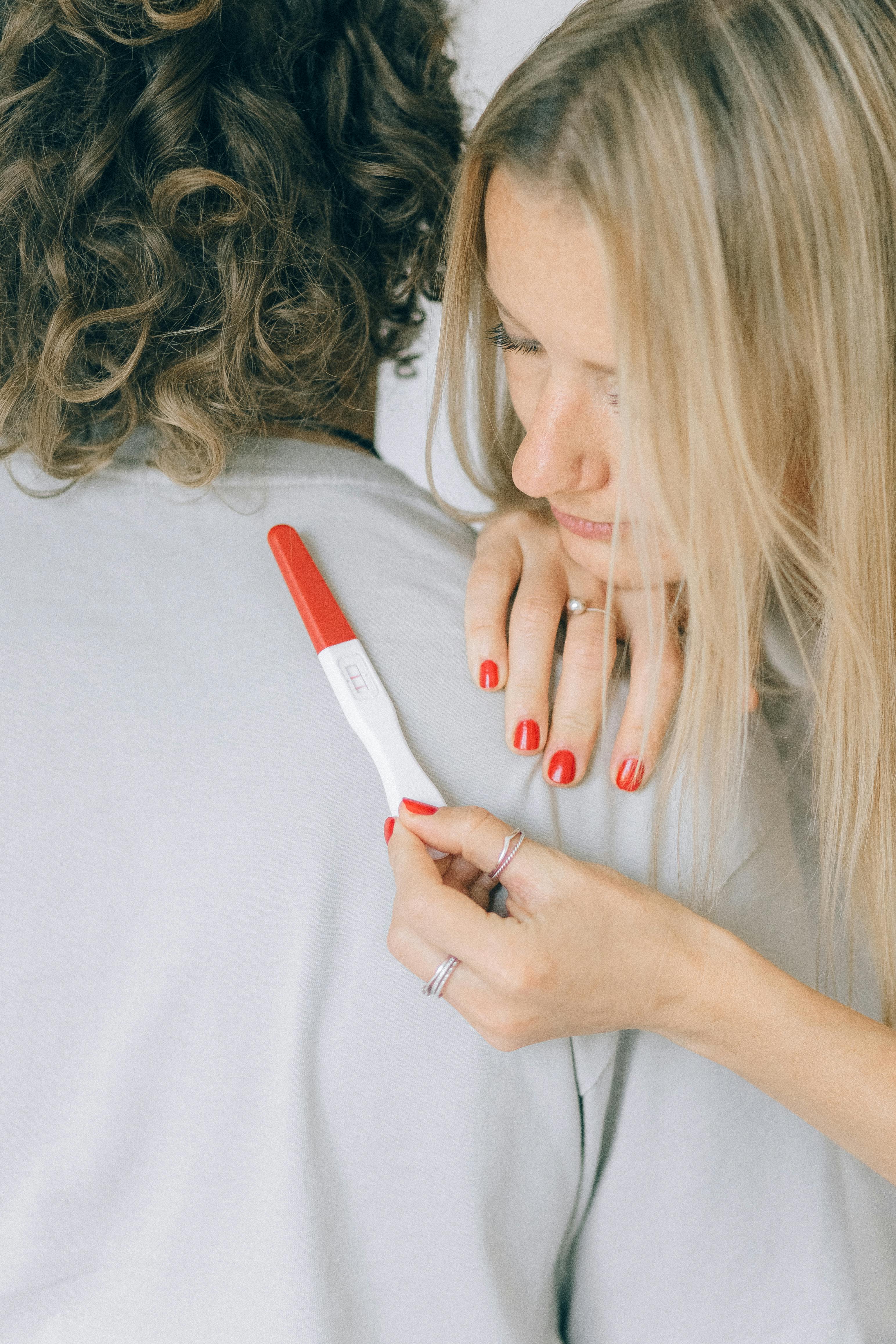 Woman hugging a man while holding a pregnancy test | Source: Pexels