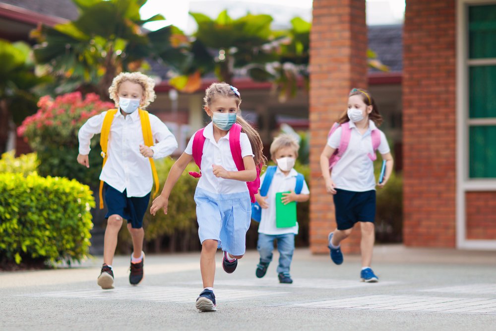 School children wearing face masks during the COVID-19 pandemic and running as they play together | Photo: Shutterstock/ FamVeld