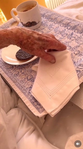 A detailed look at the tray shows a chocolate digestive resting on a small plate beside a cup of coffee, while Lady Pamela Hicks's hand gently hovers over a folded napkin. The composition highlights the thoughtful simplicity of her birthday morning routine. | Source: Instagram/indiahicksstyle