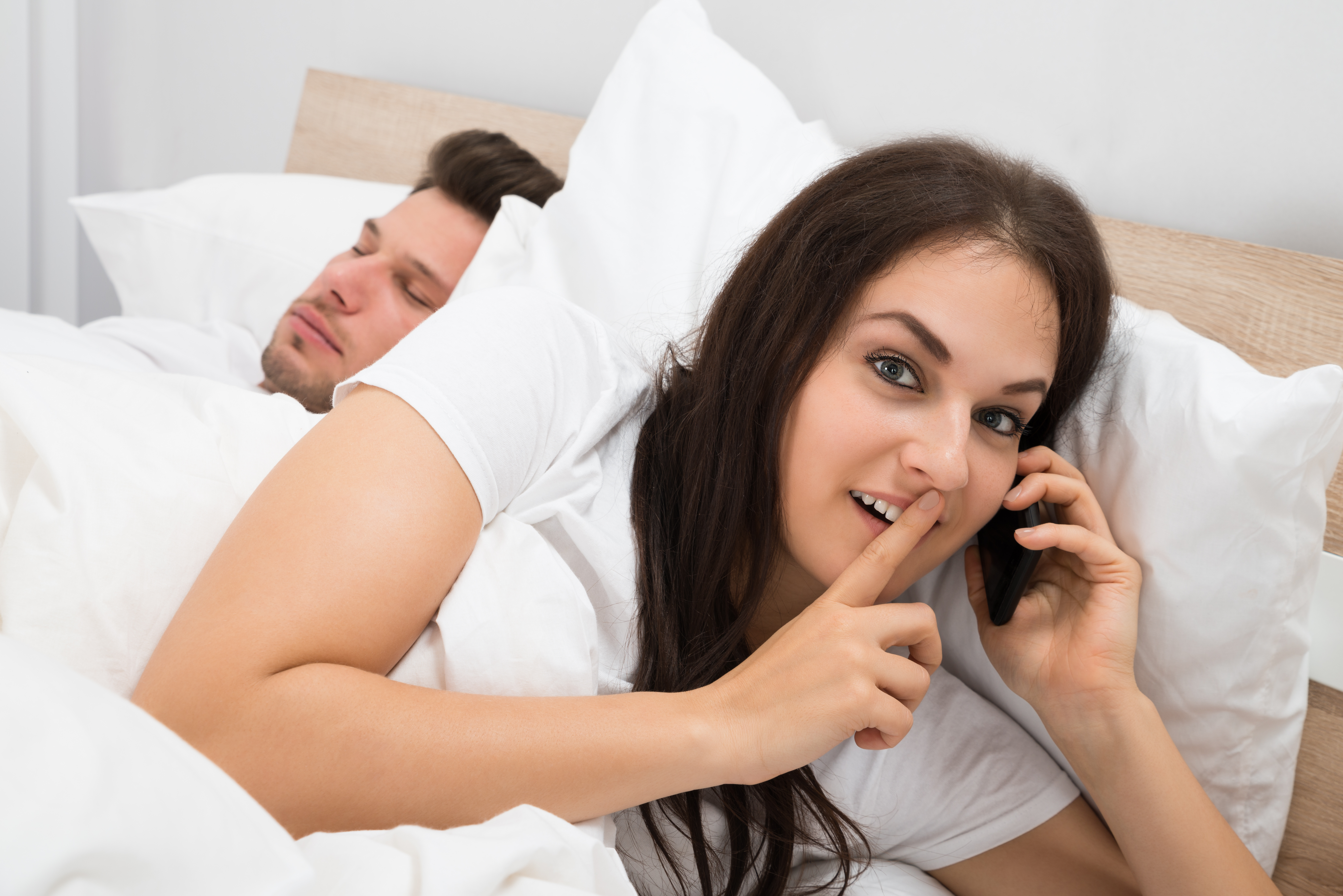 Woman taking a call while a man sleeps beside her | Source: Shutterstock